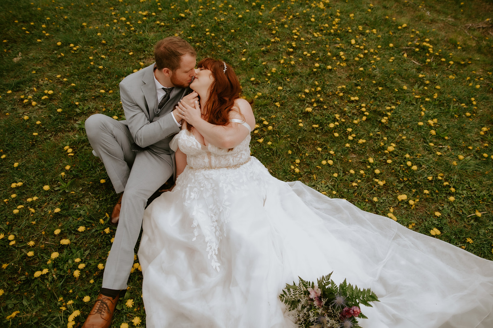 Bride and groom sitting in a grassy field covered in wildflowers, sharing a quiet kiss during their intimate elopement portraits.