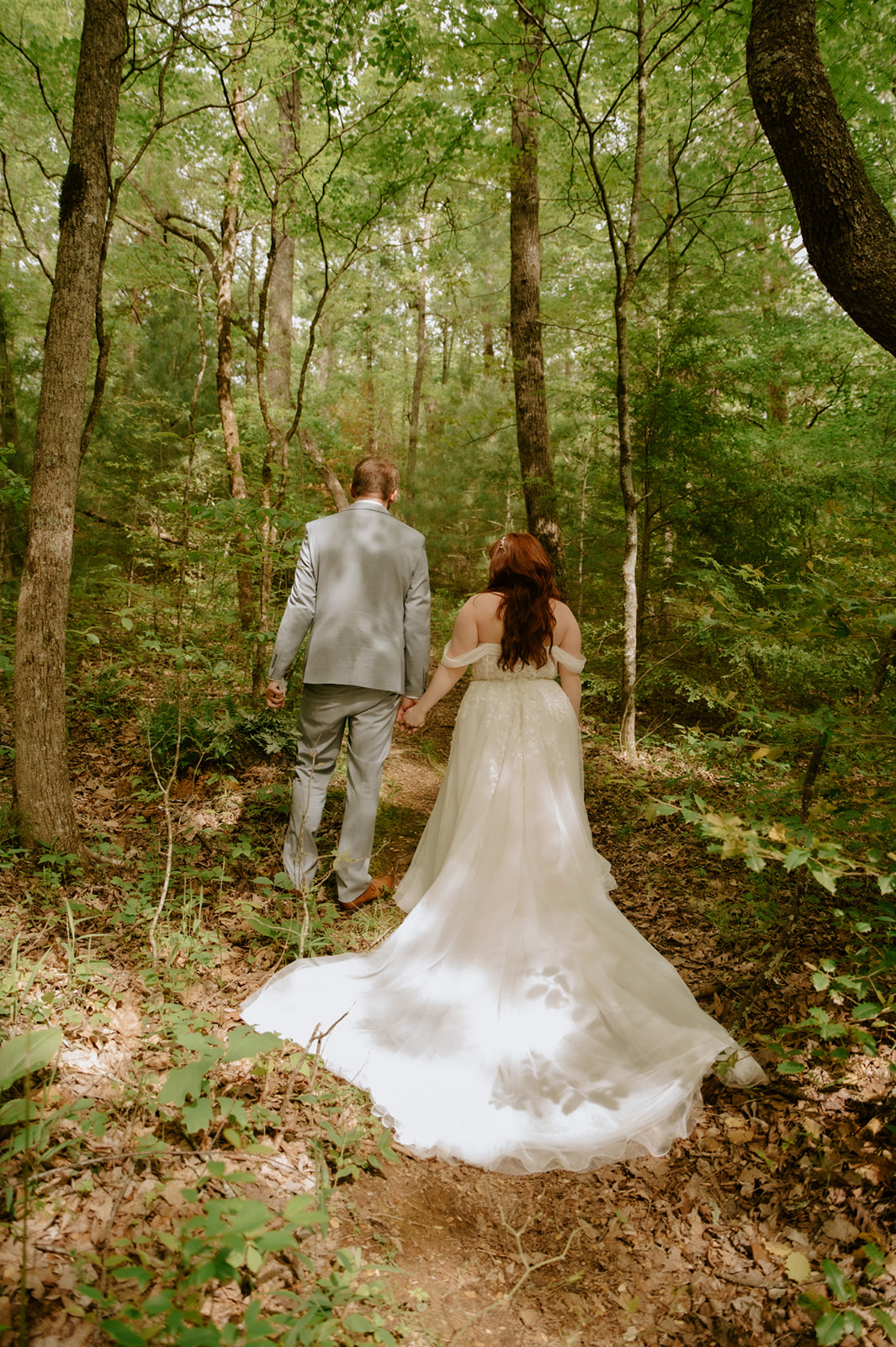 Couple walking hand in hand through a forest trail during their Smoky Mountain Elopement, with sunlight filtering through the trees.