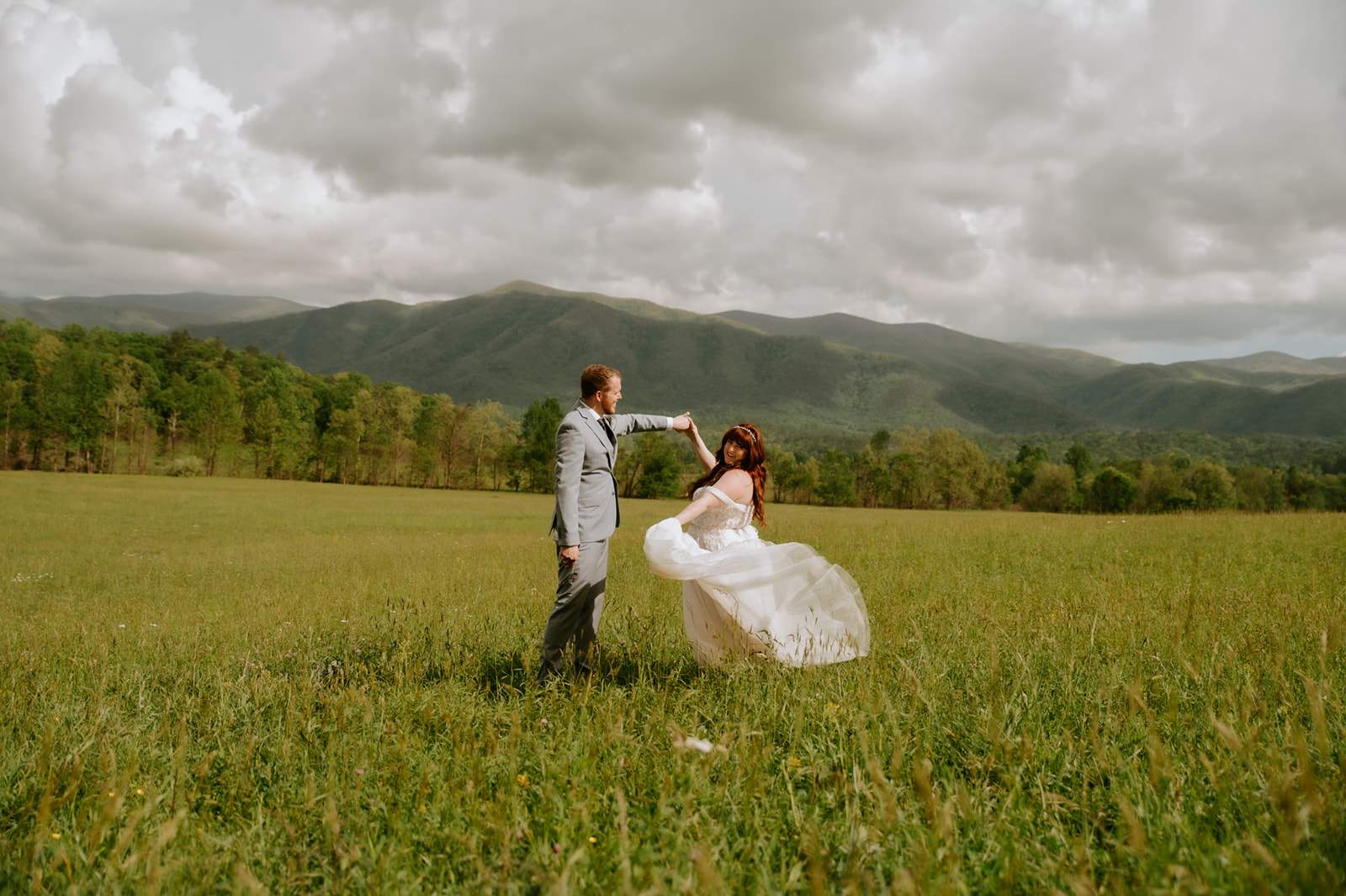 Couple twirling together in an open field with Smoky Mountain views during their elopement day
