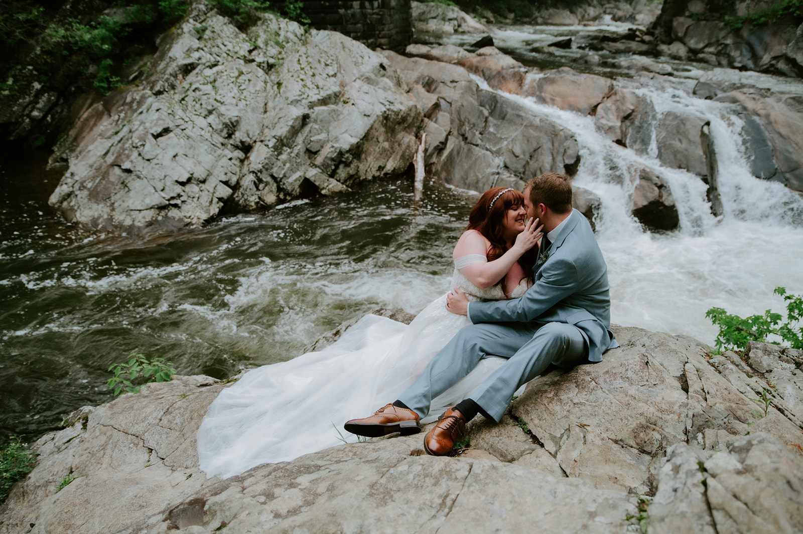 Couple sitting together on rocks by a rushing river during their Smoky Mountain elopement portrait session.