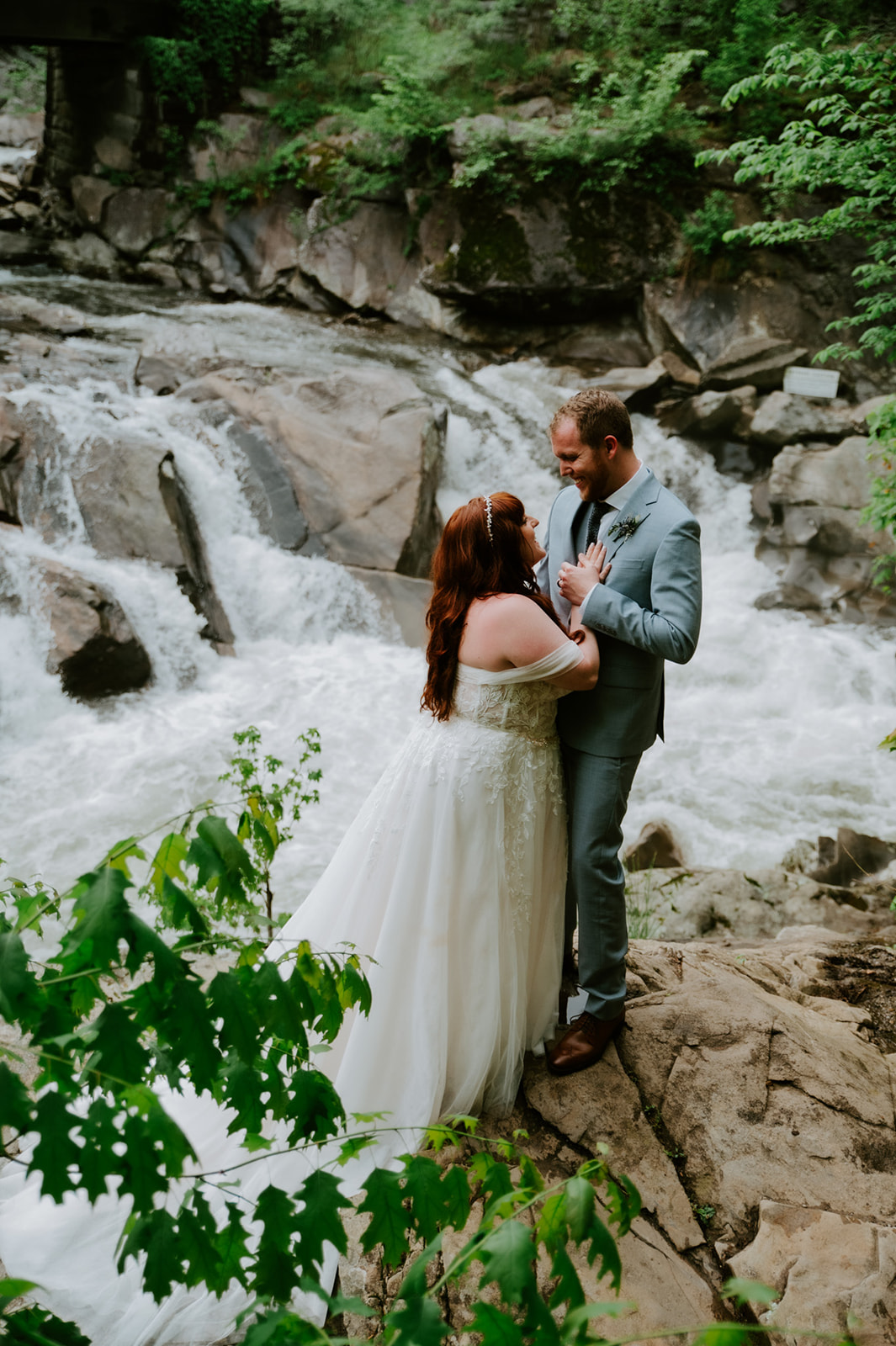Couple standing together on rocks near the river, smiling at each other between moments.
