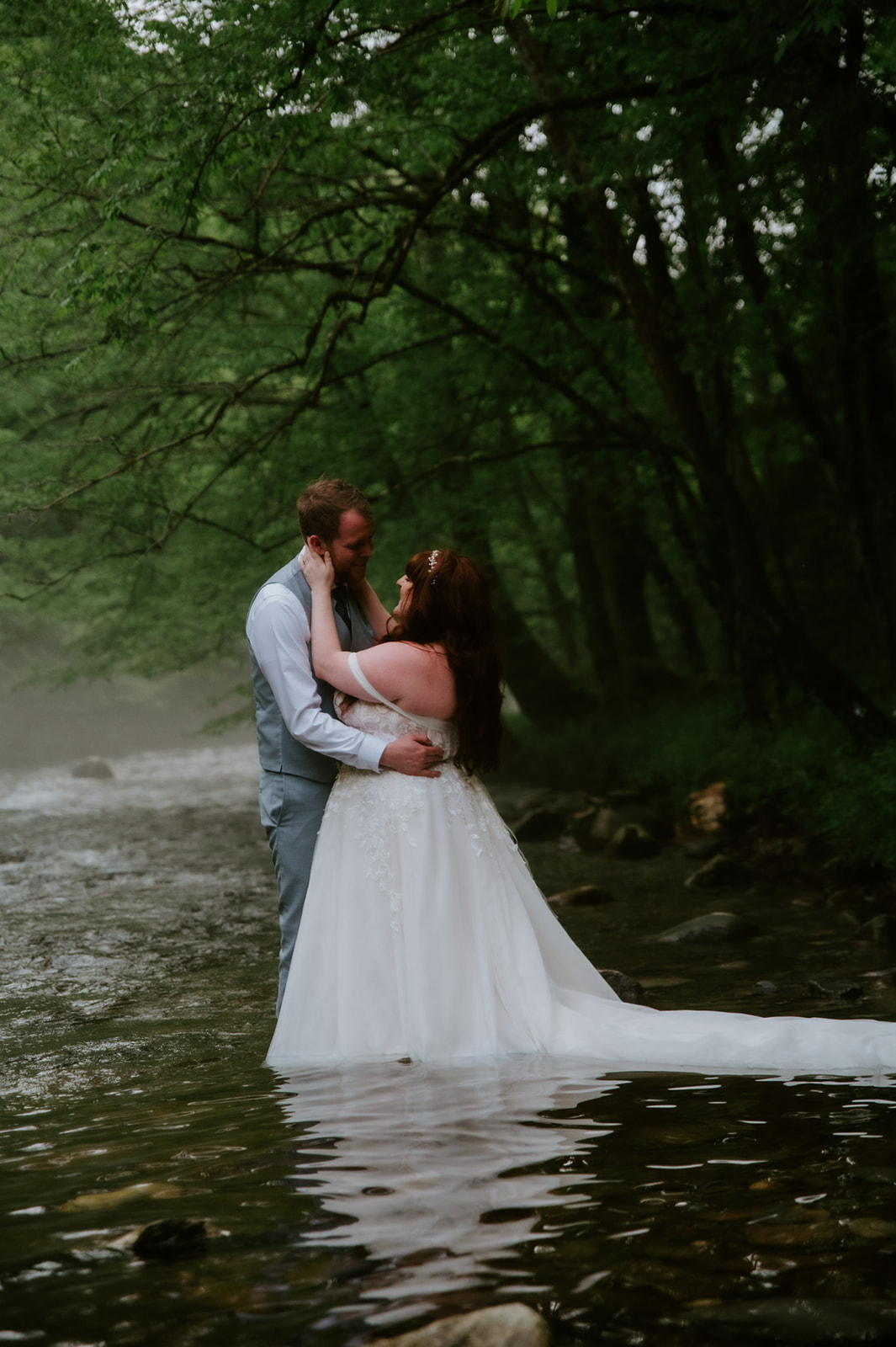 Couple embracing in the river, surrounded by mist and greenery at the end of their elopement day.