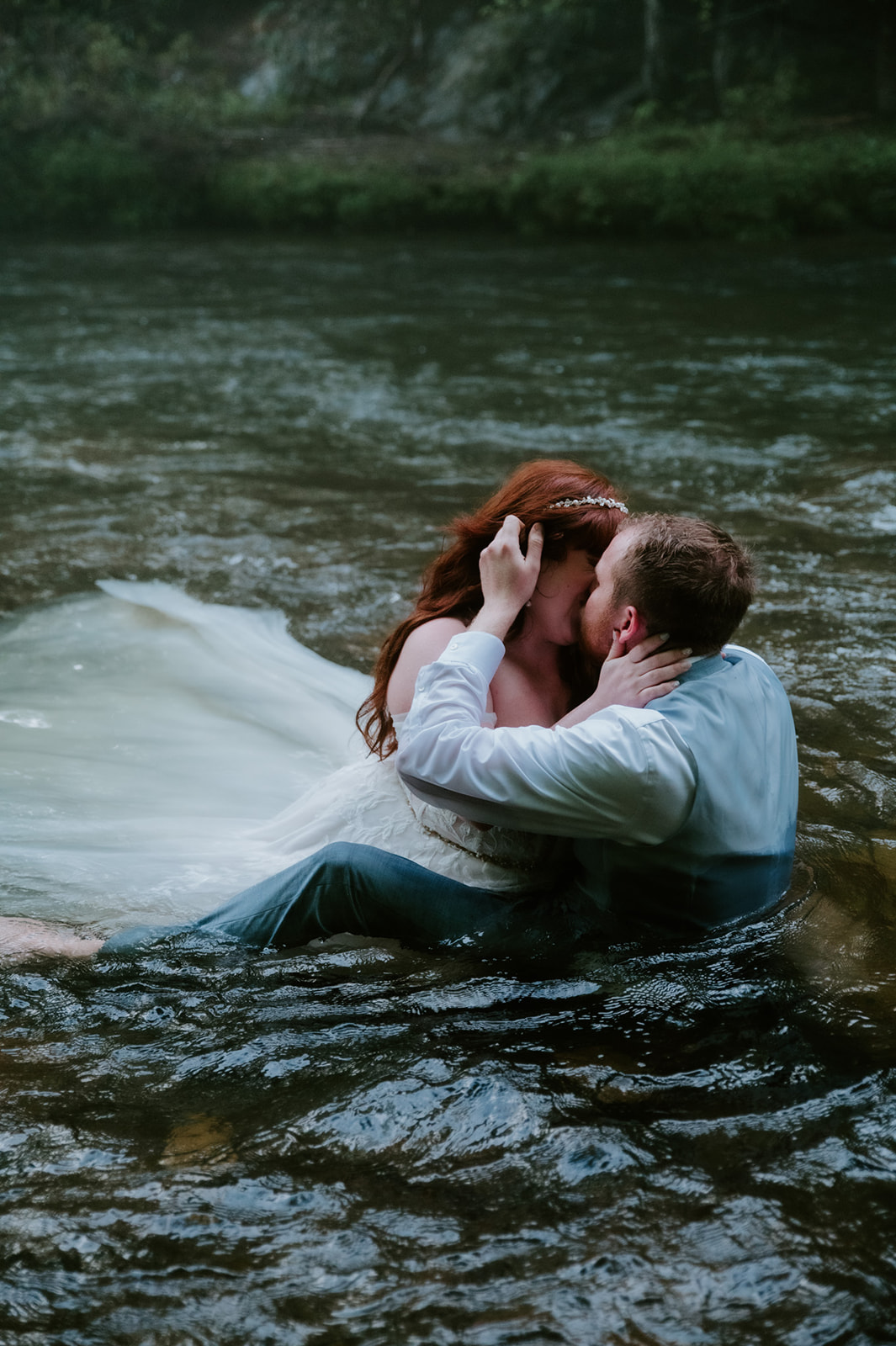 Couple kissing in a cold river during their Smoky Mountain Elopement, fully dressed and embracing the adventure at the end of the day.