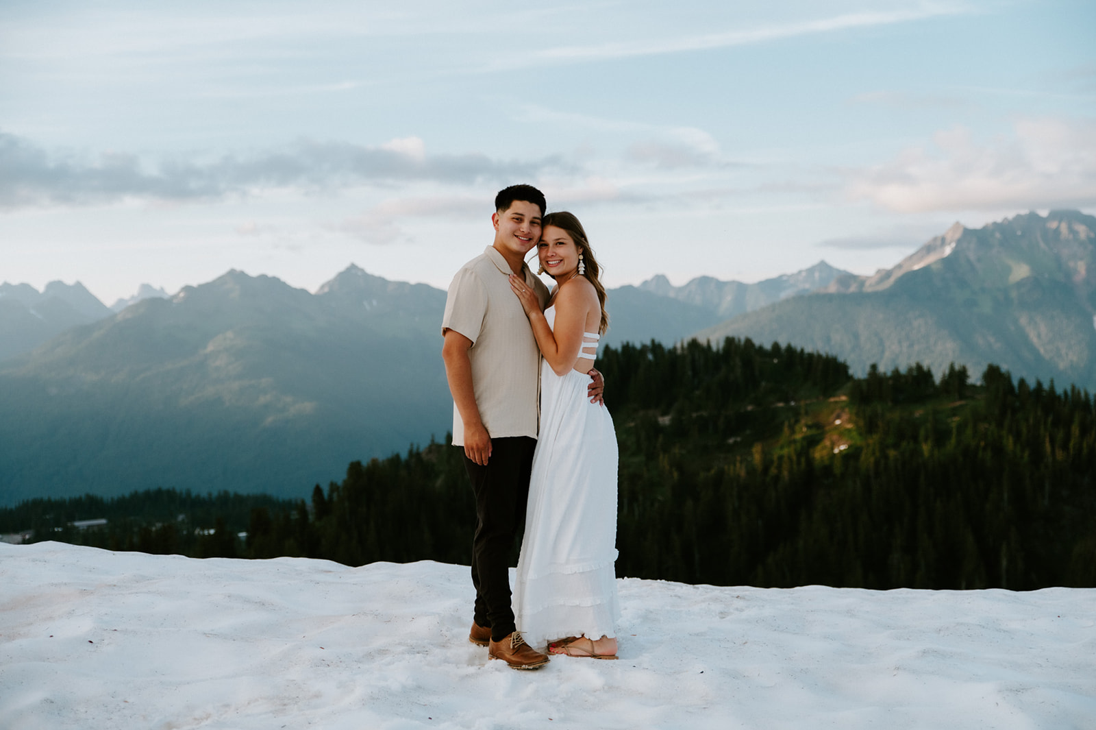 Couple smiling together on a snowy overlook as they elope in Washington, framed by layered mountain ridgelines.