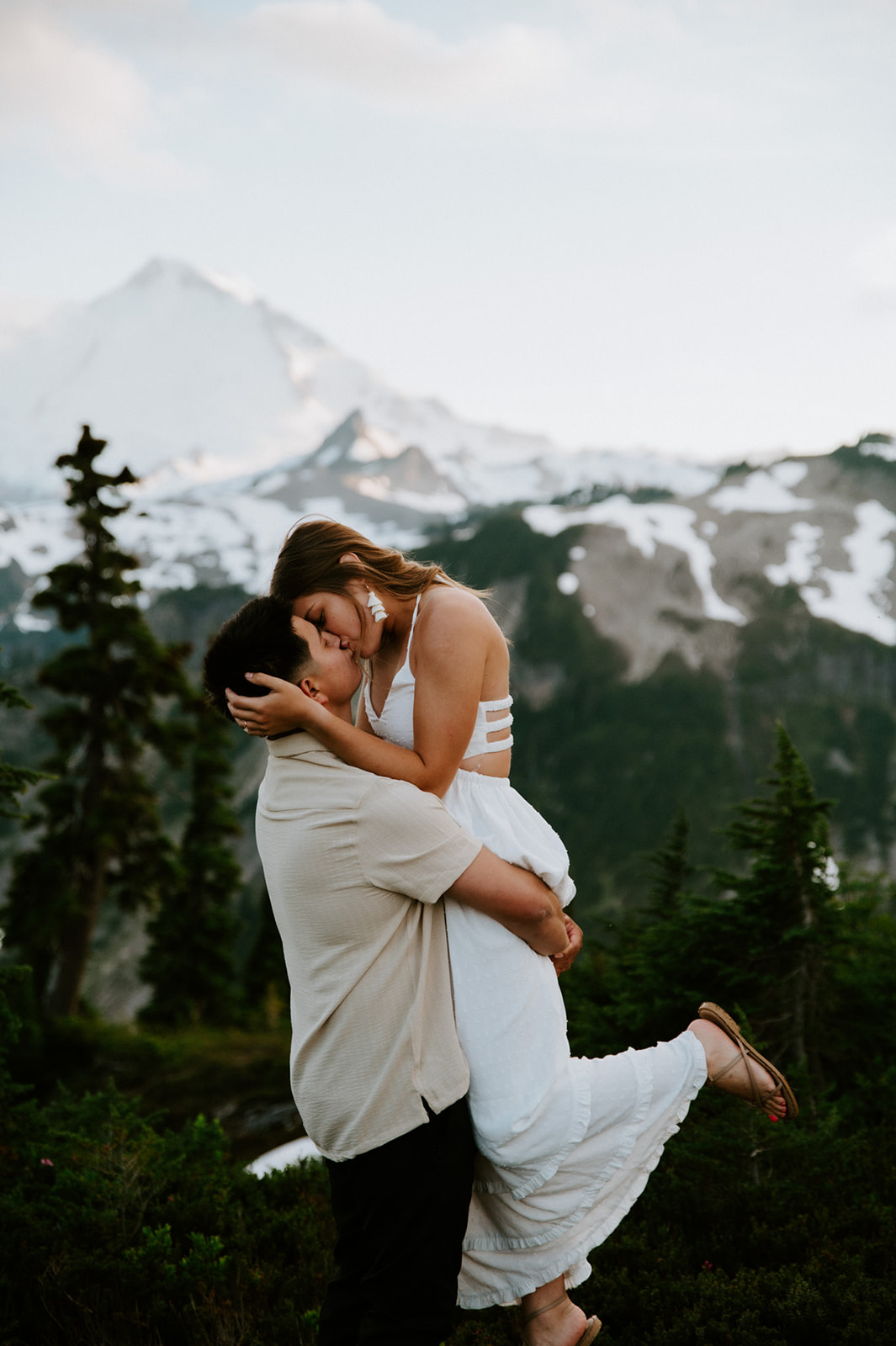 Couple sharing a lifted hug and kiss on a mountain ridge while they elope in Washington, with dramatic peaks in the distance.