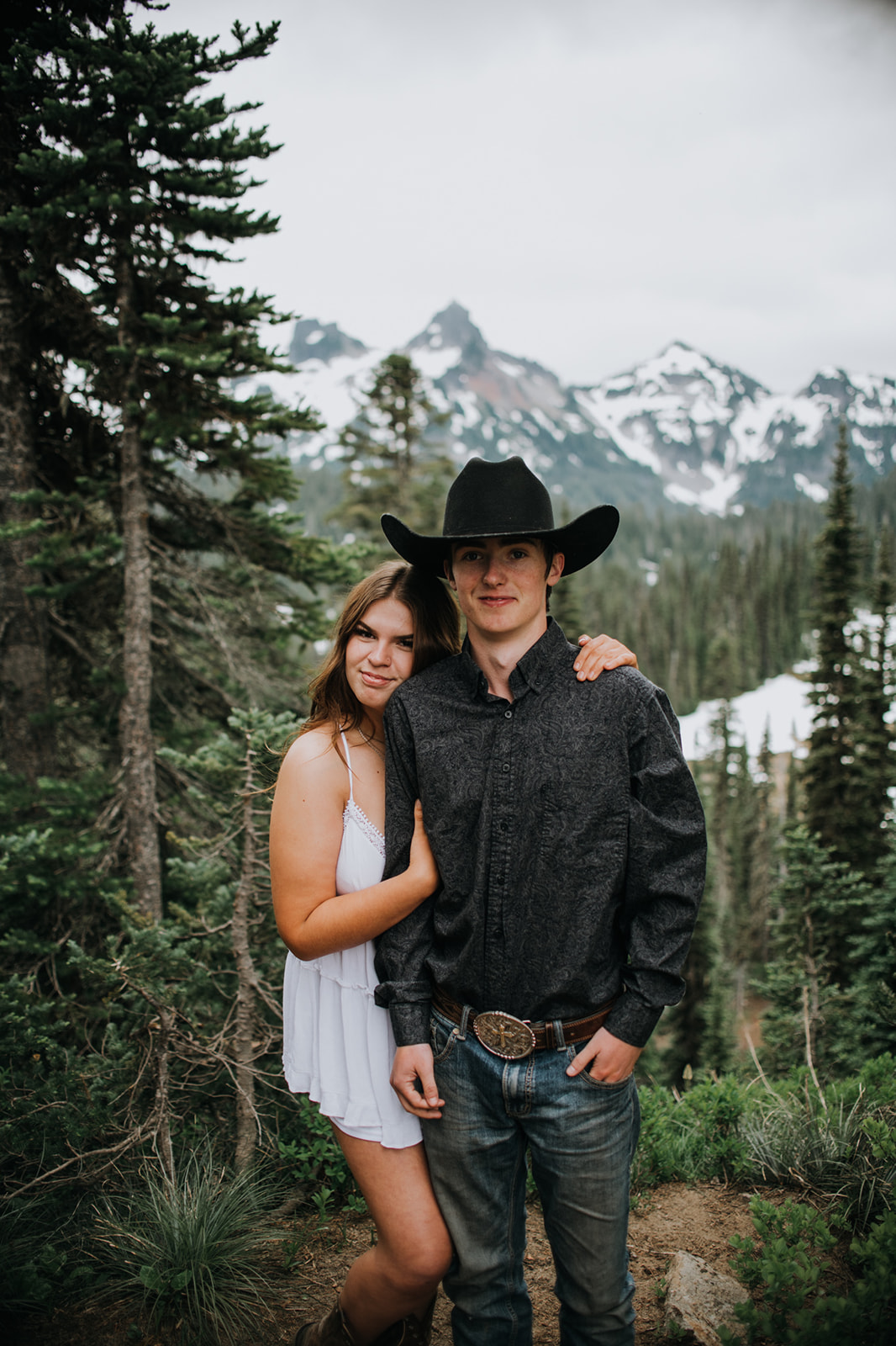 Couple posing together in front of evergreen trees and rugged mountain peaks while they elope in Washington in a quiet alpine setting.