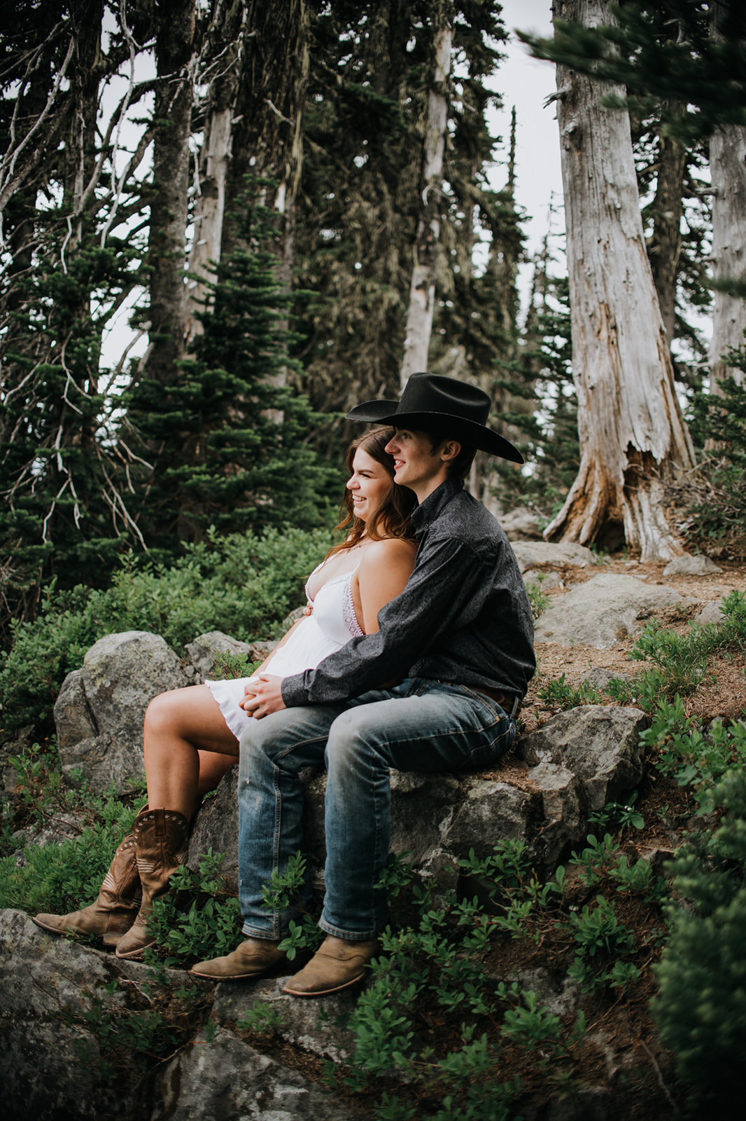 Couple sitting together on a rock in the woods, relaxed and smiling during a casual mountain elopement in Washington.