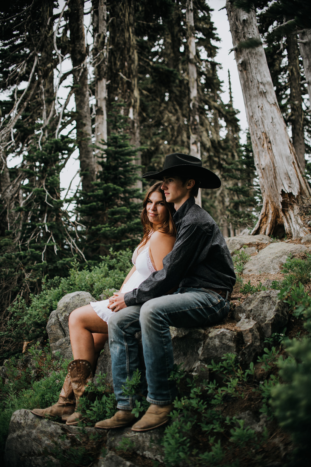 Couple sitting together on a mossy rock in a quiet forest clearing during a relaxed Washington elopement.