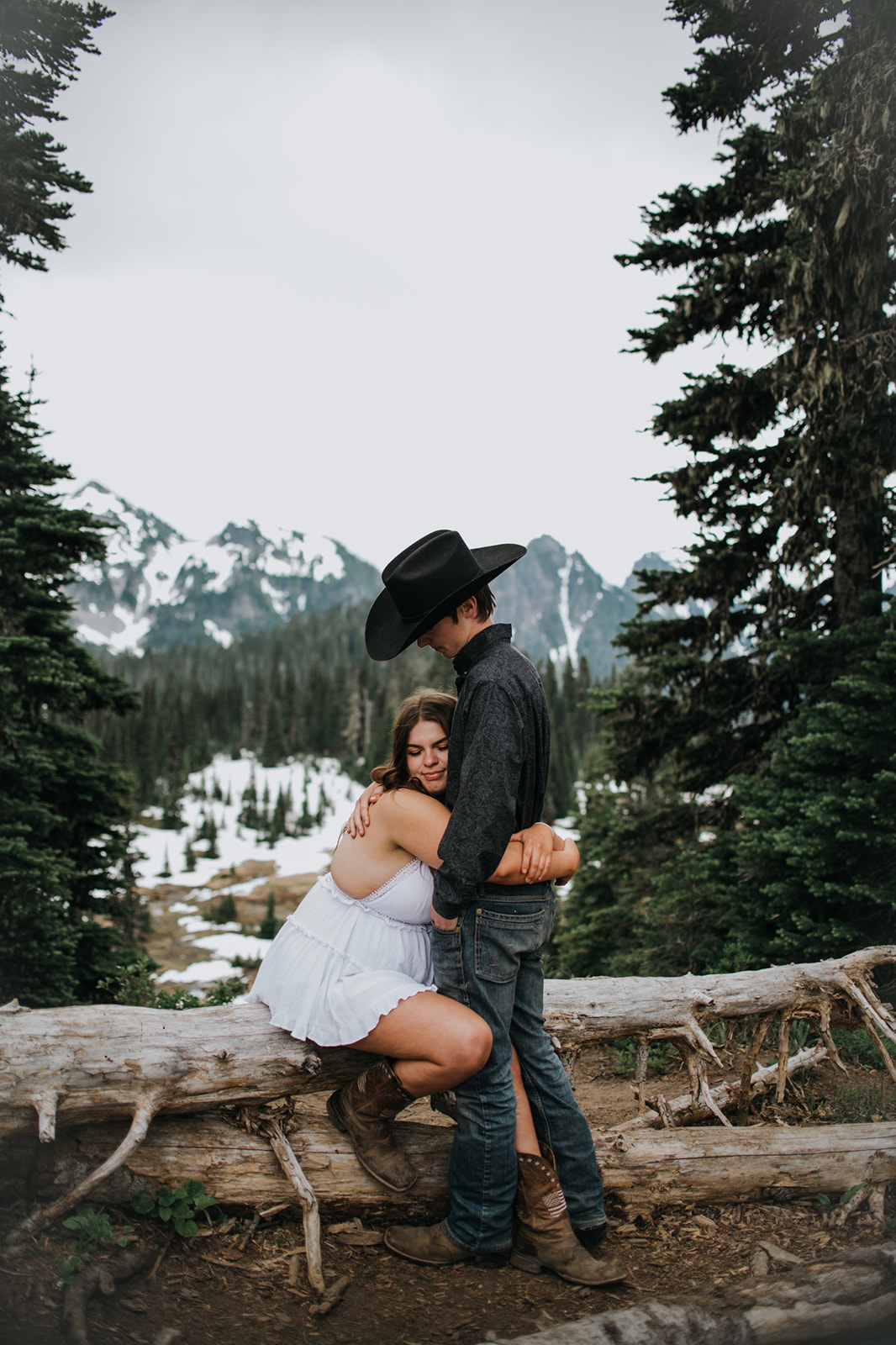 Couple sharing an intimate moment on a fallen log surrounded by evergreen trees during a relaxed Washington elopement.