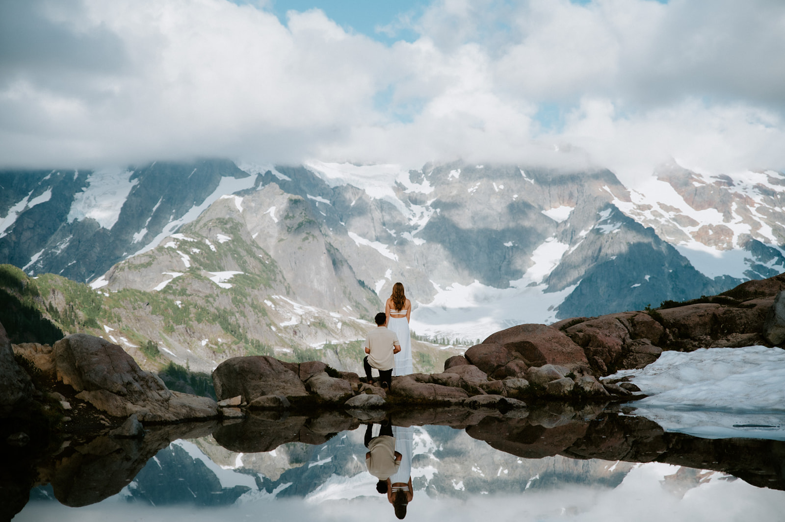 North Cascades elopement couple standing at a mountain overlook with snow-covered peaks reflected in an alpine lake