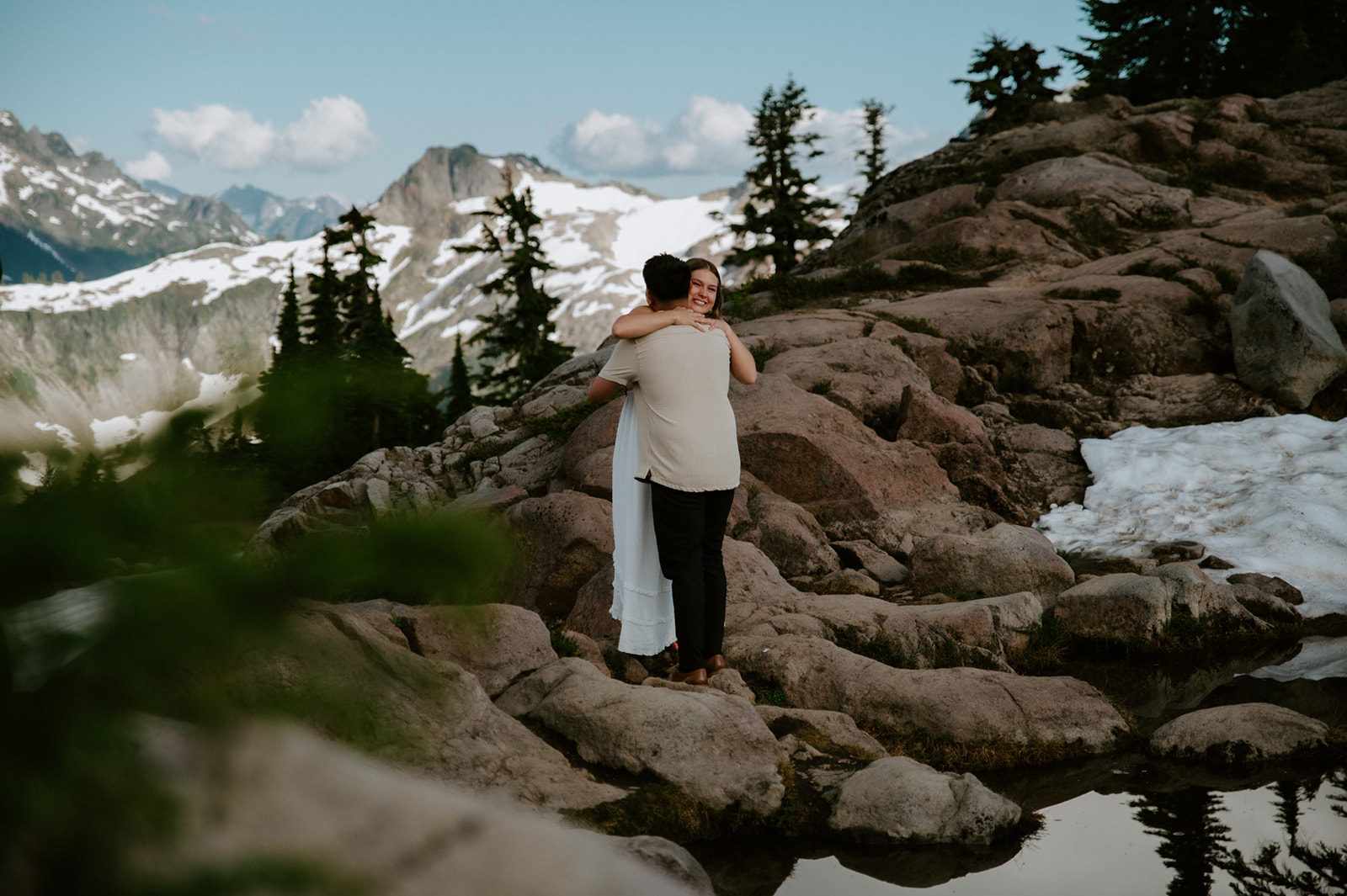 Couple hugging on a mountain overlook after proposal with alpine rocks and snowfields during their north cascades elopement
