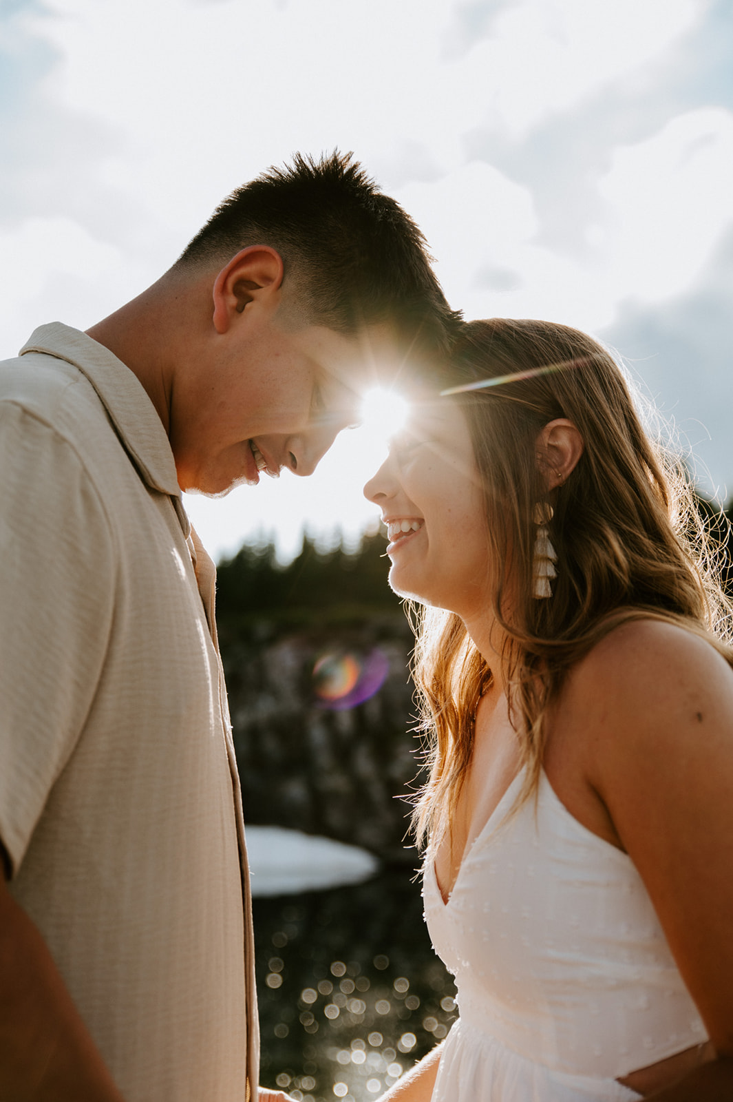 Backlit couple laughing forehead-to-forehead with sun flare over alpine lake during North Cascades elopement