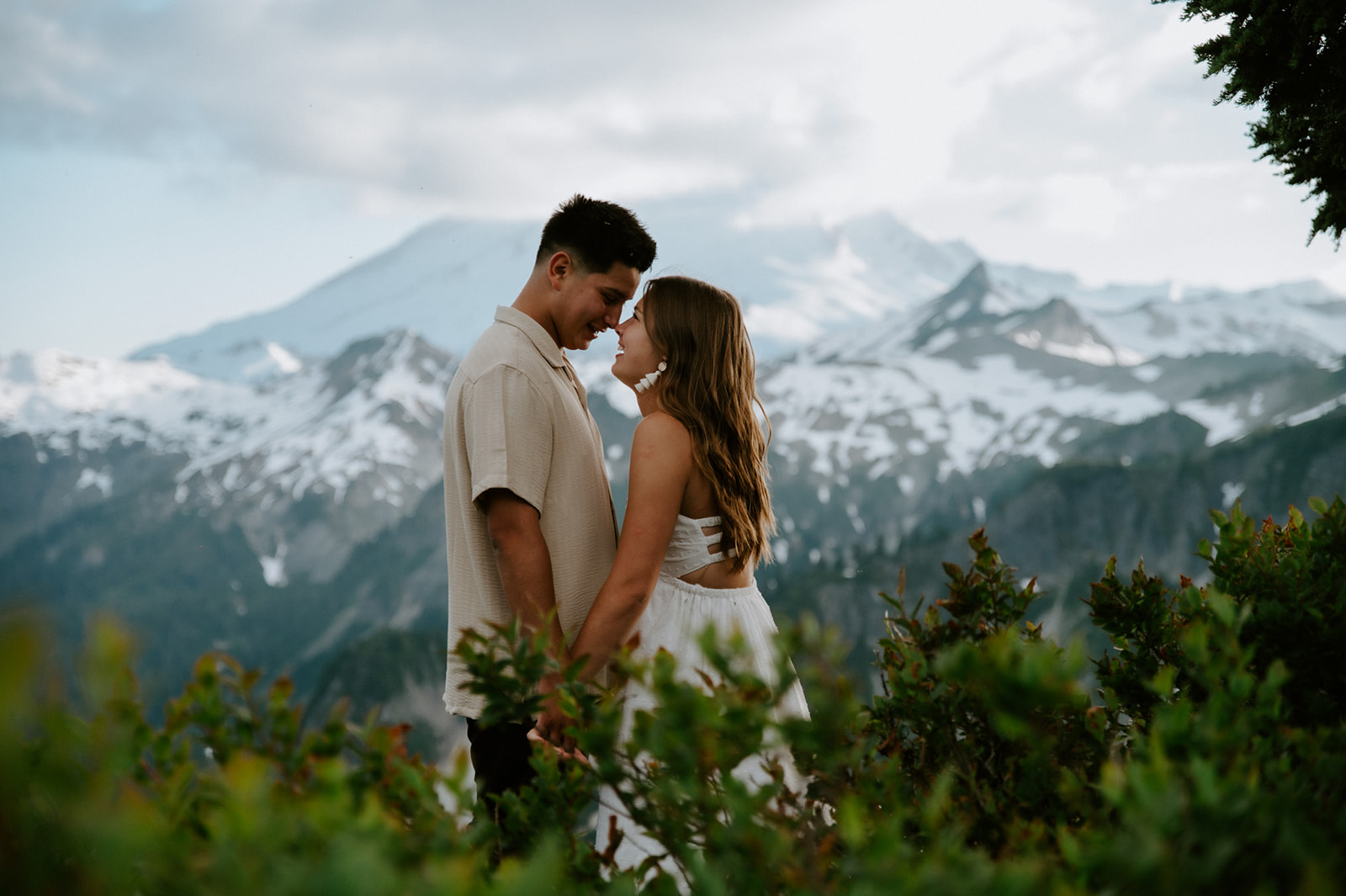 North Cascades elopement portrait of couple standing close together with layered mountain ridges and snowfields behind them