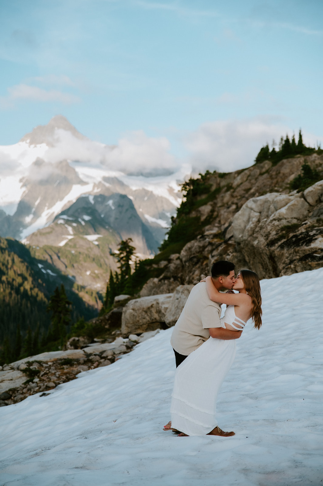North Cascades elopement couple kissing on a snow-covered ridge with rugged peaks and clouds overhead