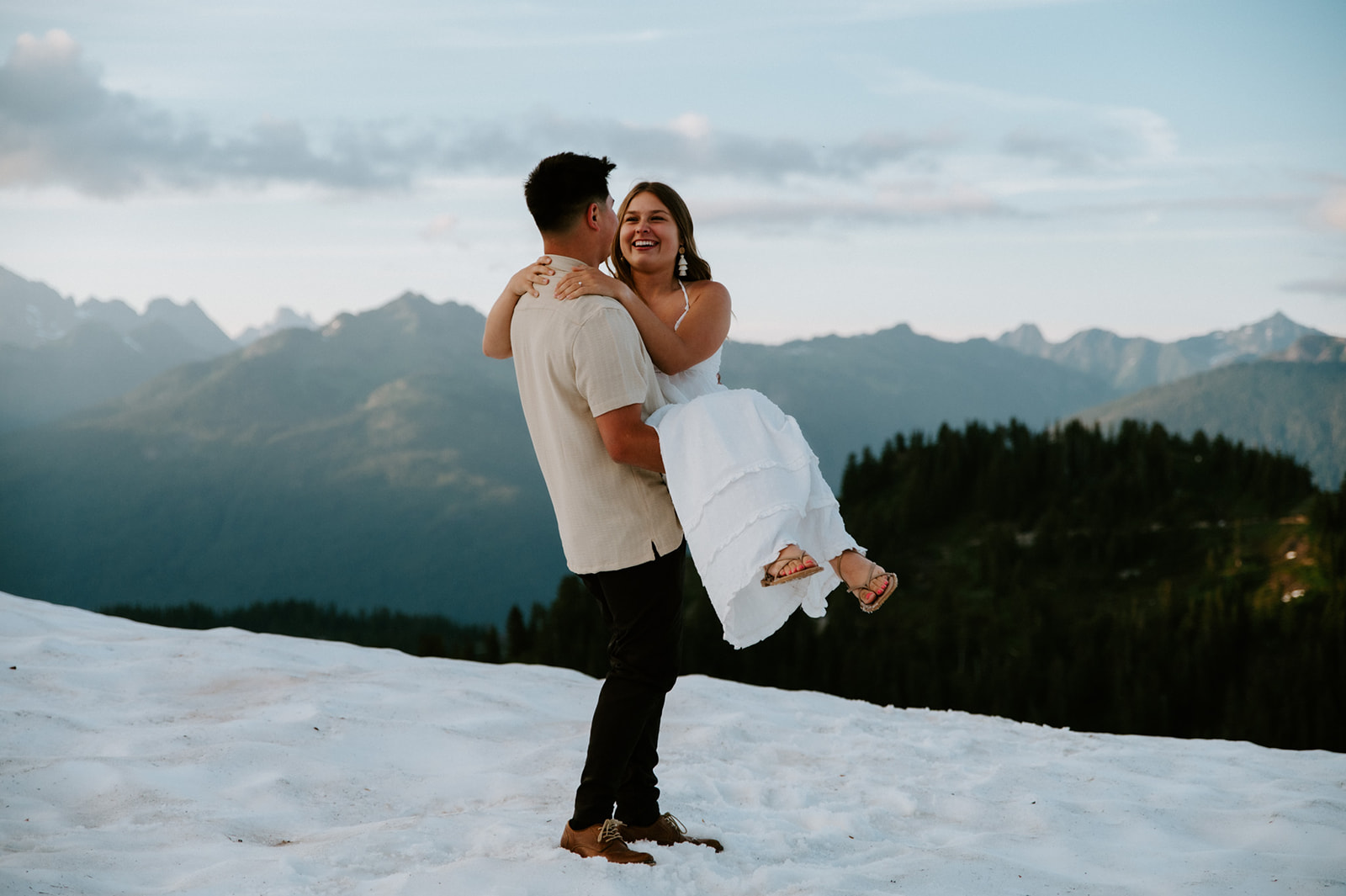 Couple hugging on a mountain overlook after proposal with alpine rocks and snowfields during their north cascades elopement