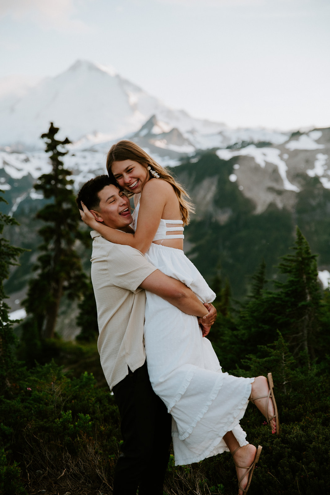 Playful mountain engagement moment as couple hugs and laughs above the tree line in Washington