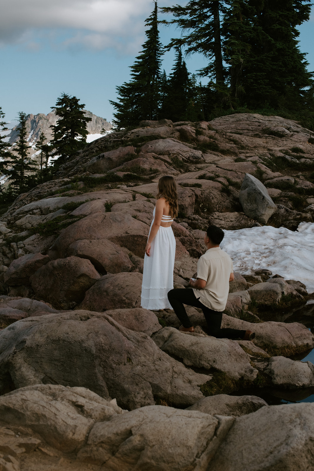 Man kneeling to propose on rocky mountain terrain with lingering snow during a north cascades elopement hike