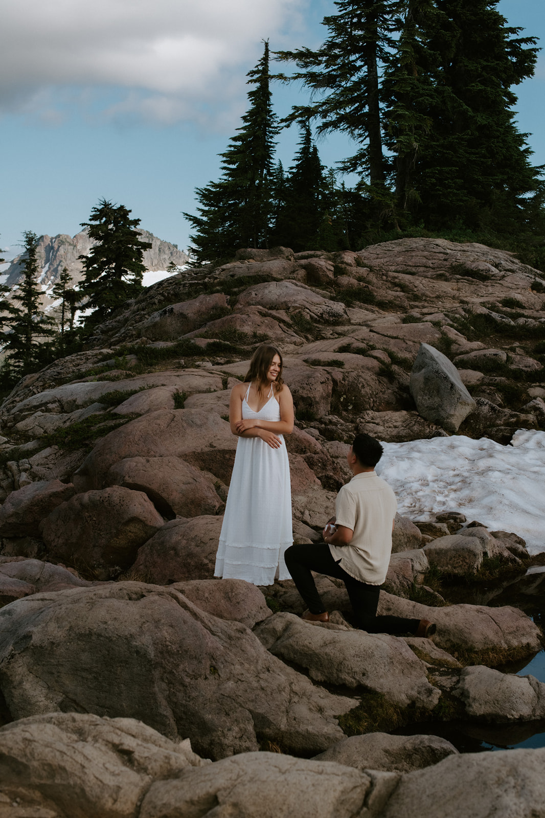 Surprise proposal moment on a rocky ridge with snow patches and evergreen trees during a north cascades elopement