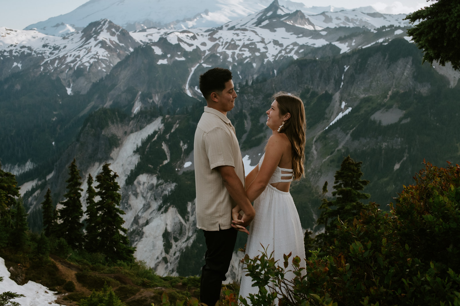 North Cascades elopement couple holding hands and smiling on a high elevation overlook with glacier-covered peaks