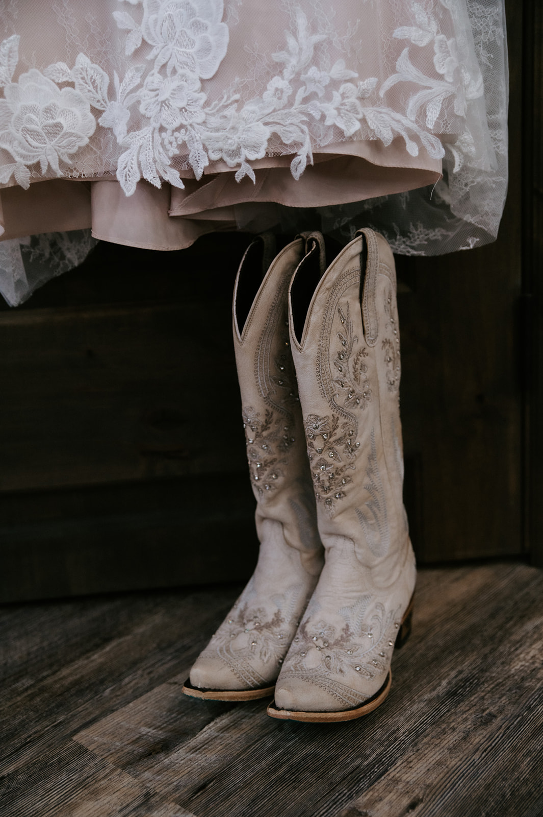 Bride’s embroidered cowboy boots placed beneath a lace wedding dress inside a cozy cabin before she elopes in Arizona.