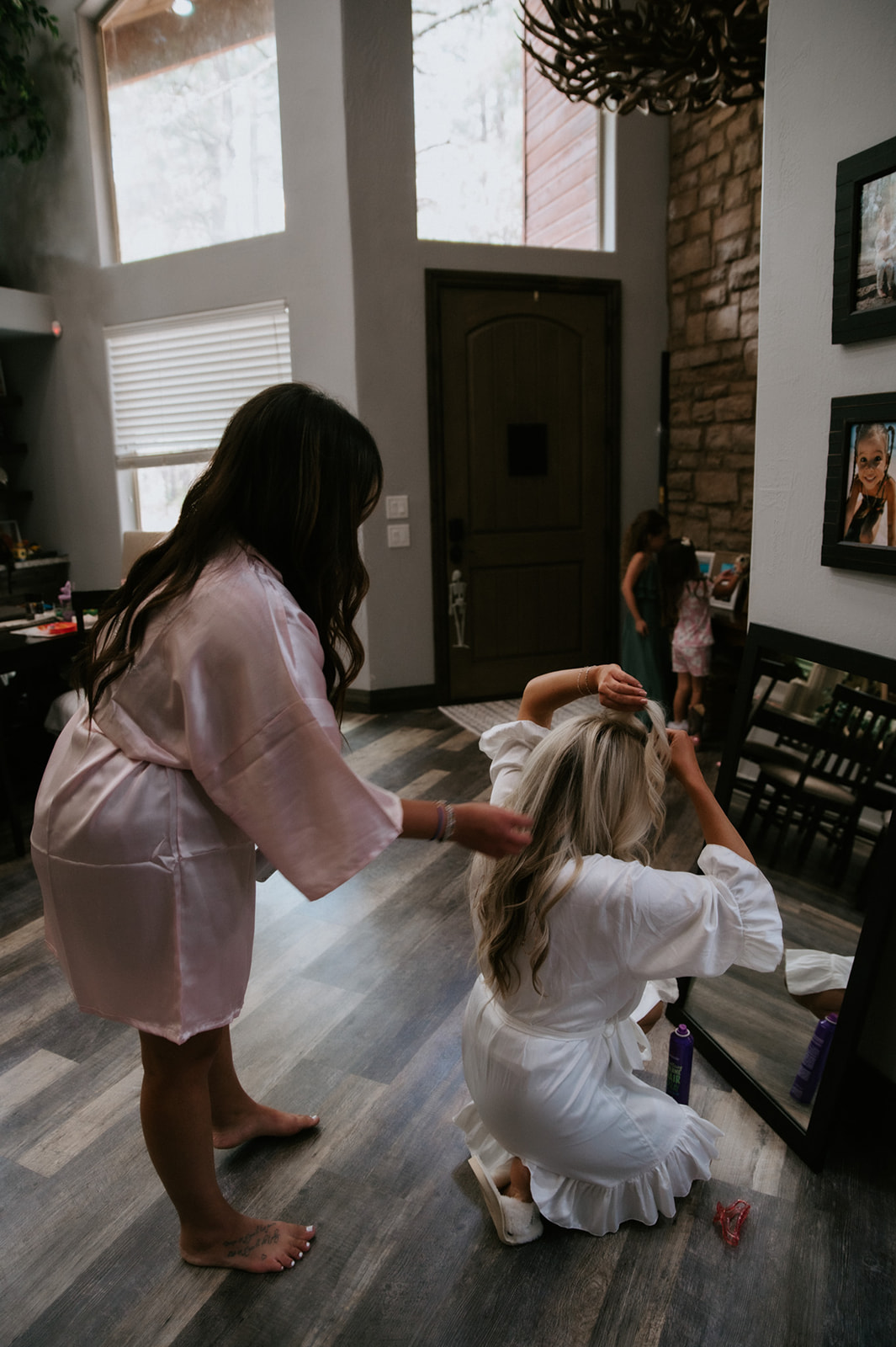 Bride sitting on the cabin floor while a bridesmaid helps with her hair before they head into the woods to elope in Arizona.