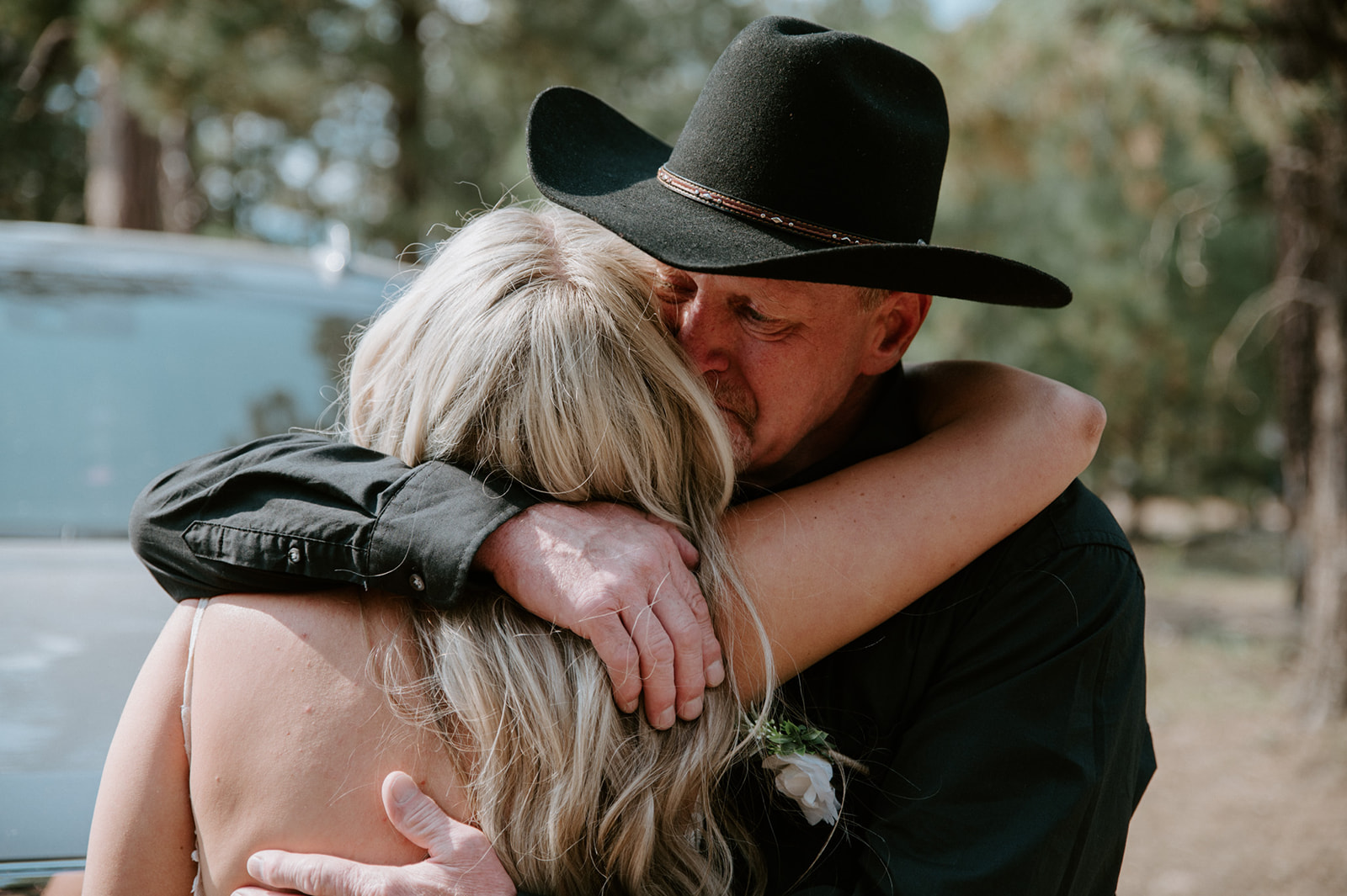 Emotional hug between bride and a family member in a cowboy hat during an intimate Arizona forest wedding day.