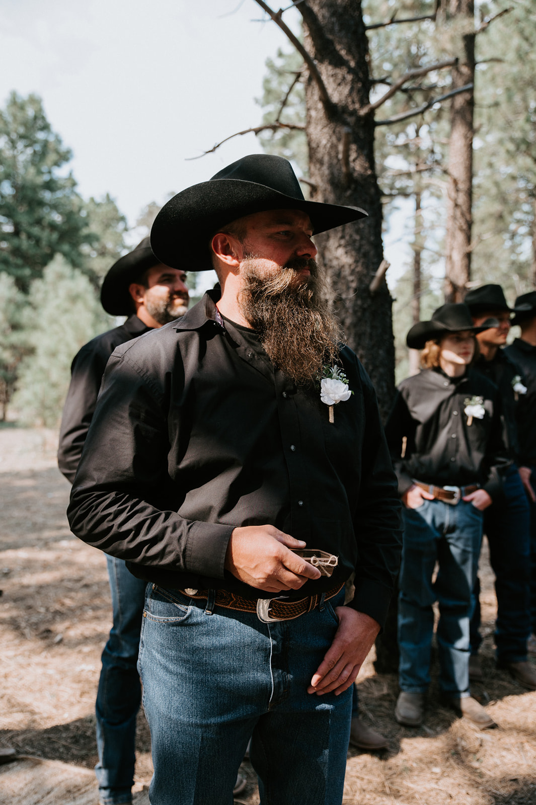 Groom and groomsmen in black cowboy hats standing in a pine forest before the couple elopes in Arizona.