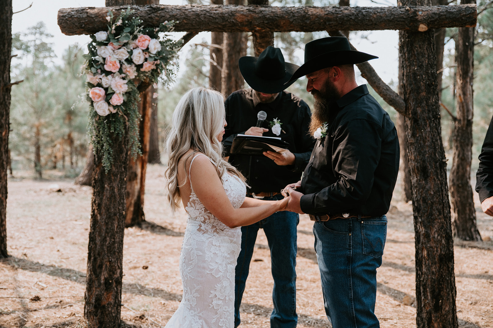 Couple exchanging vows beneath a rustic wooden arbor decorated with blush and white florals during their ceremony to elope in Arizona.