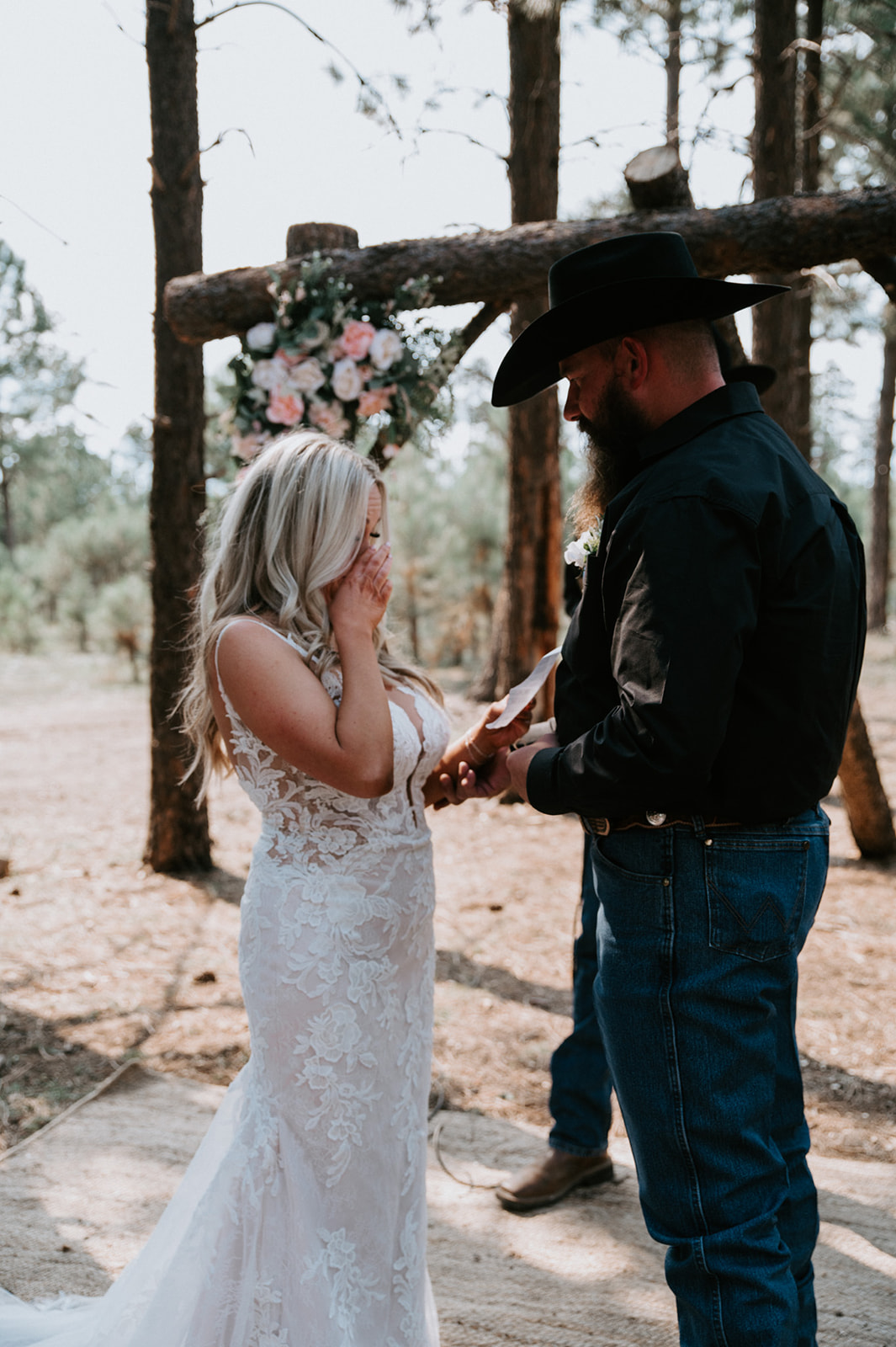 Bride wiping away tears while reading vows beneath a rustic wooden arch during their decision to elope in Arizona.