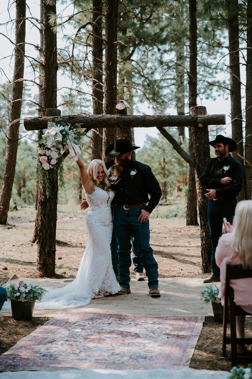 Bride celebrating under a pine arbor after the ceremony while guests look on during an Arizona forest wedding.