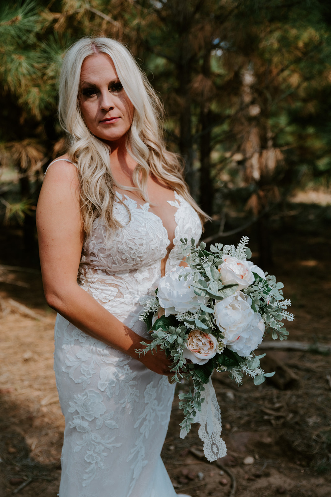 Bride holding a white and blush bouquet in a pine forest during her outdoor ceremony after choosing to elope in Arizona.