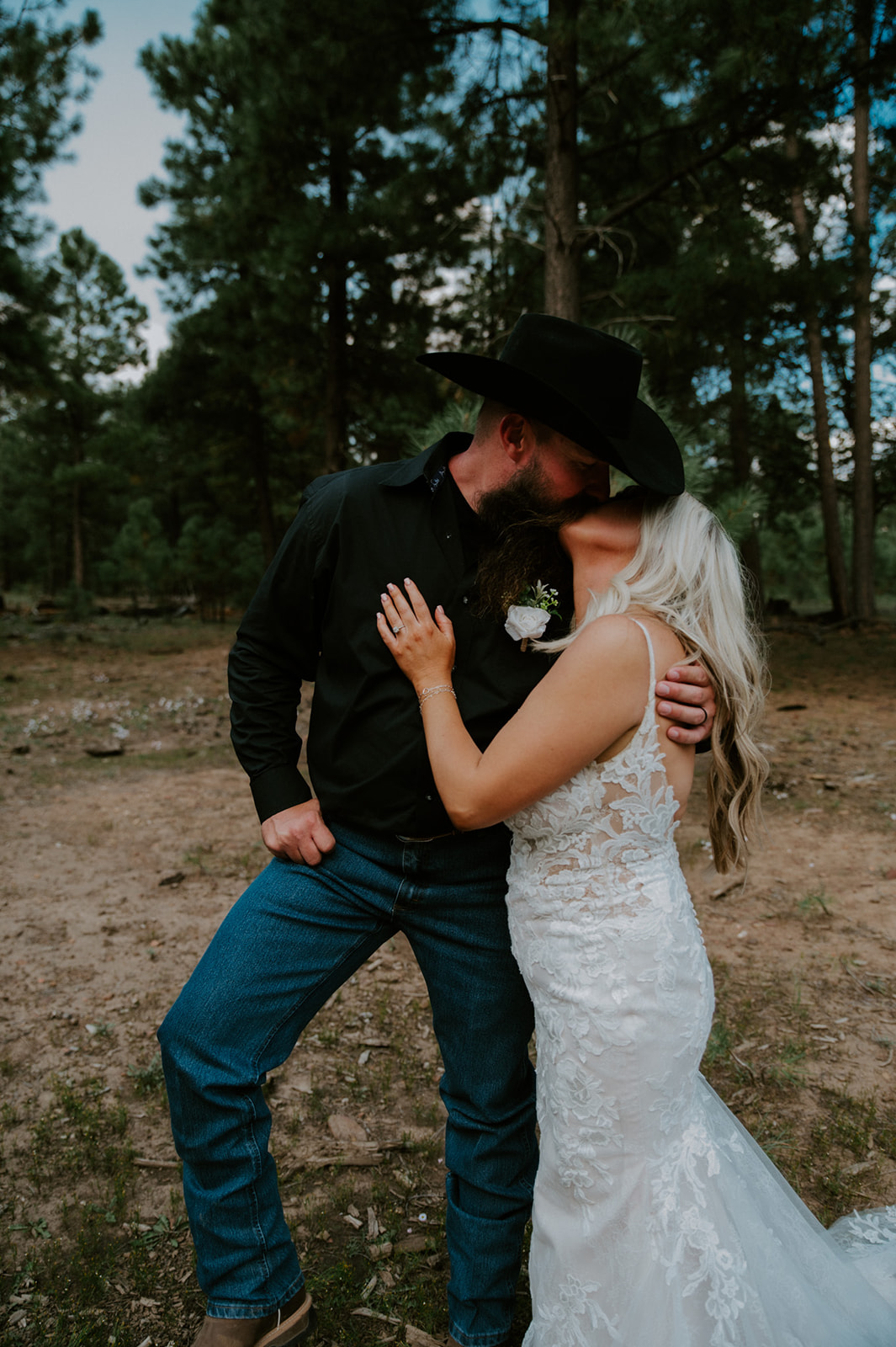 Bride and groom in western attire embracing in a quiet pine forest clearing as they elope in Arizona.