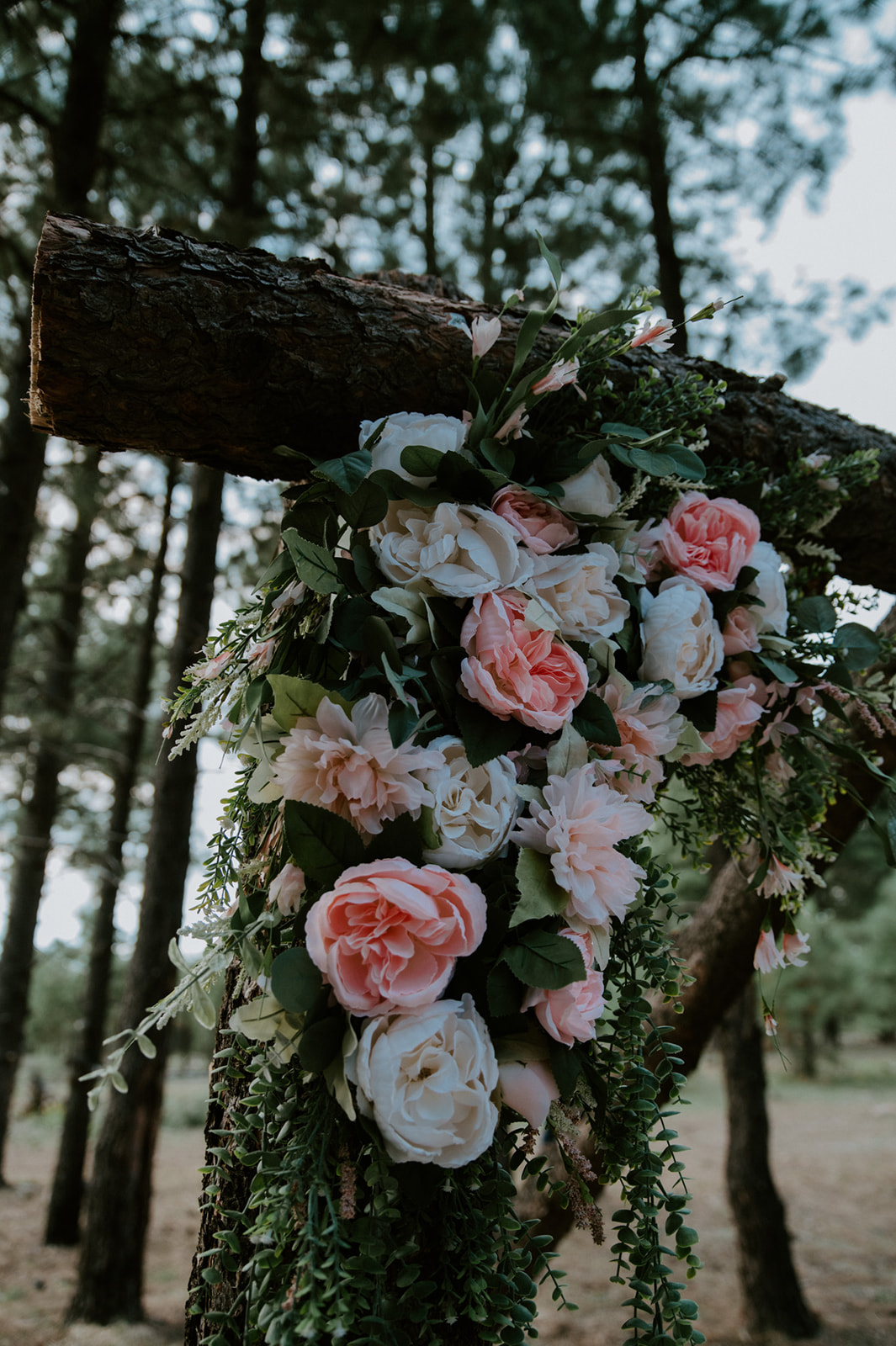 Close-up of blush and ivory florals draped over a wooden ceremony arch during a forest elopement in Arizona.