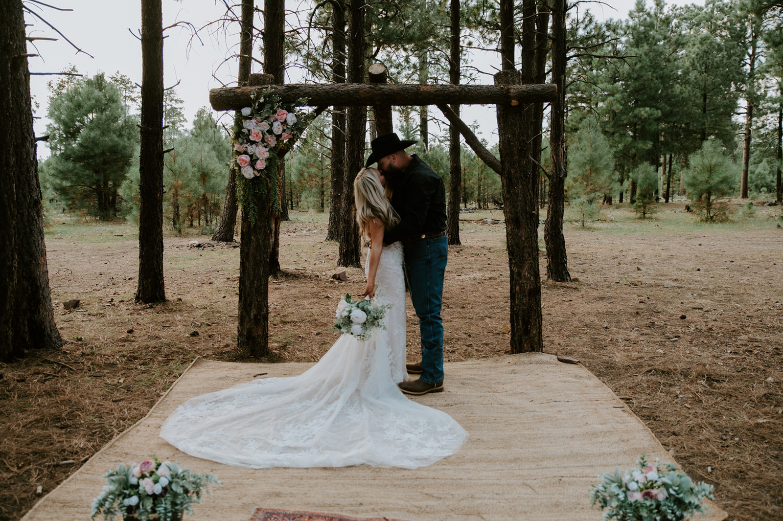 Bride and groom embracing beneath a rustic wooden arbor in the pine forest after choosing to elope in Arizona.