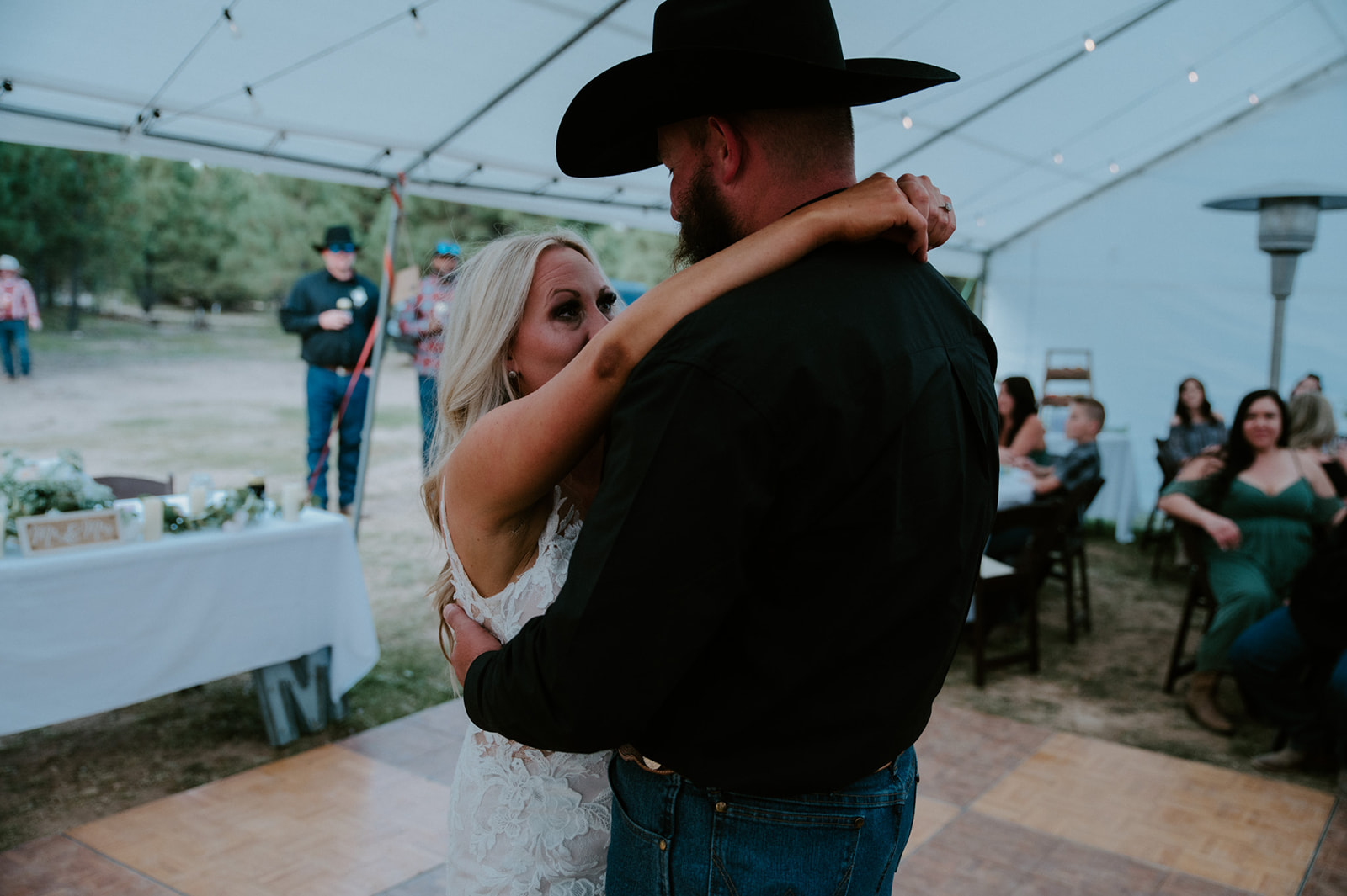 Bride looking up at groom while slow dancing under string lights at their intimate forest wedding reception.