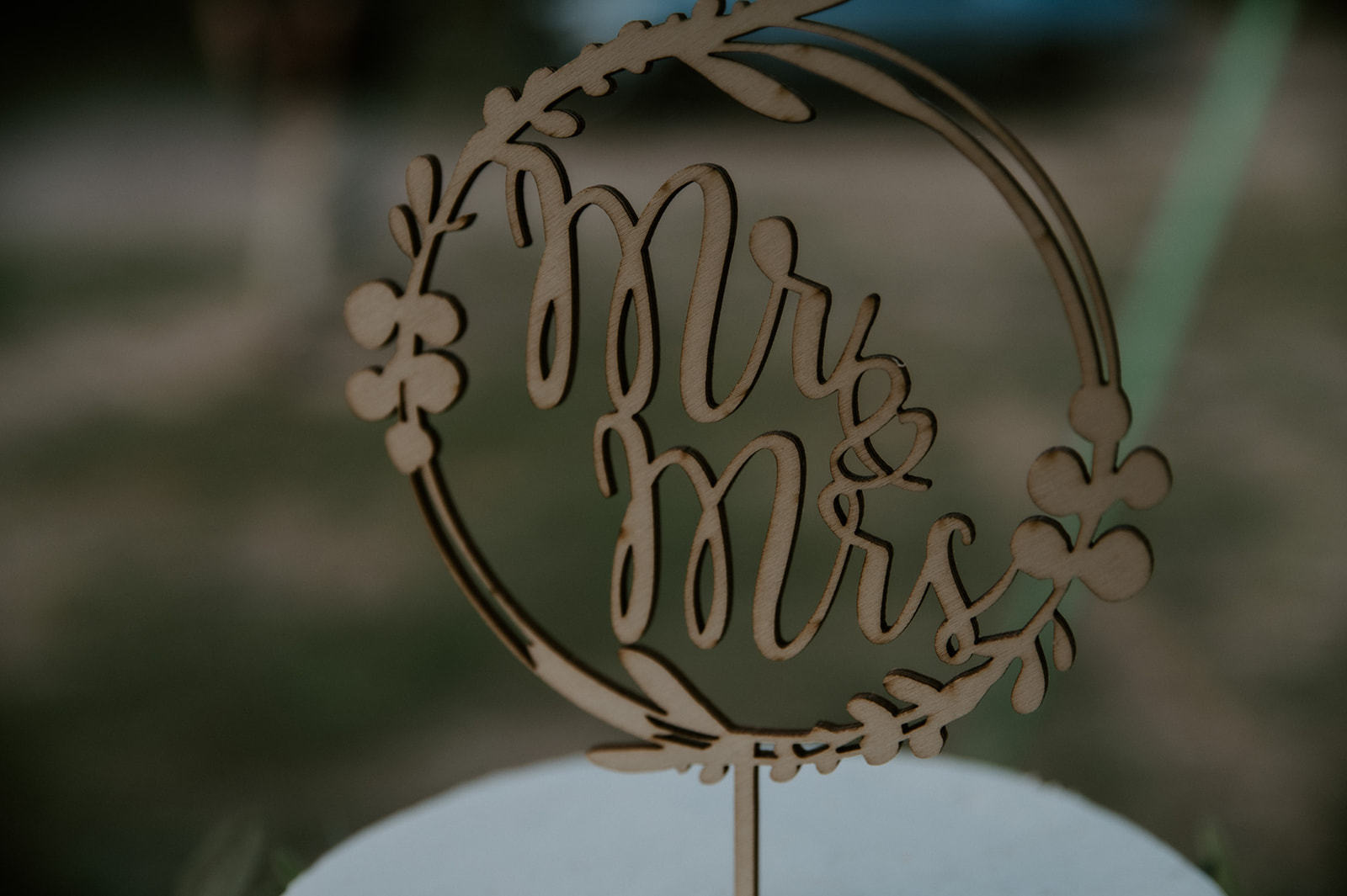 Close-up of wooden “Mr & Mrs” cake topper displayed on a simple white wedding cake at a forest reception in Arizona.