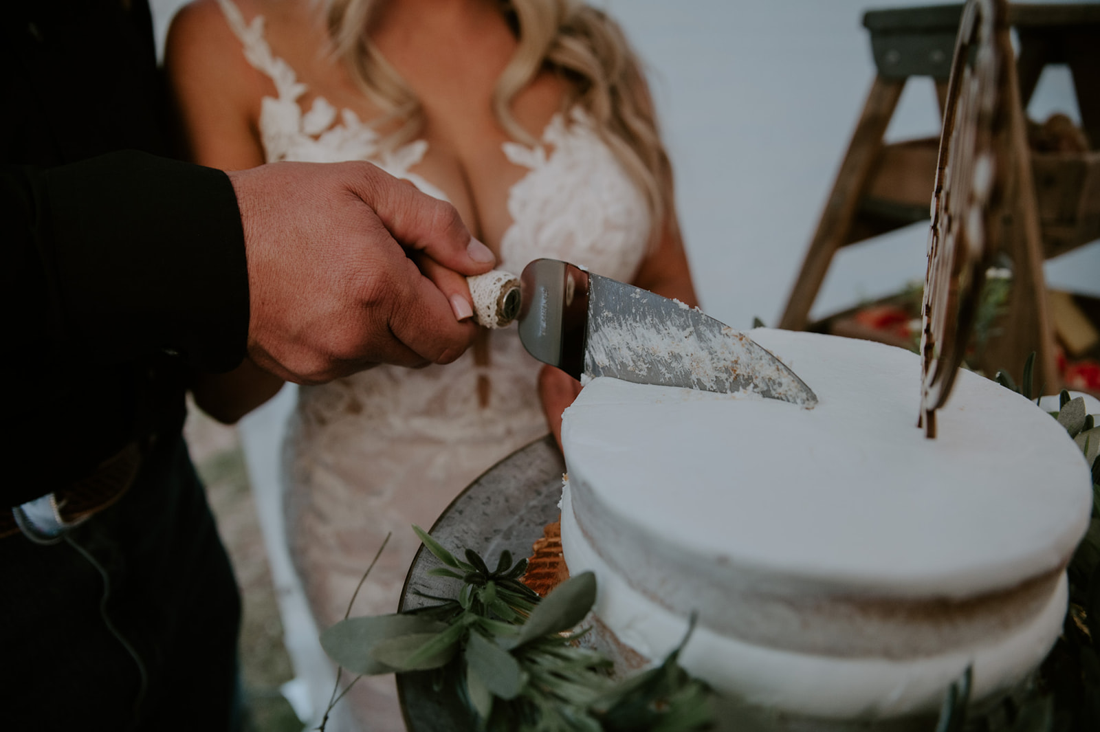 Close-up of groom cutting into a minimalist white cake with rustic knife during an intimate Arizona forest wedding.