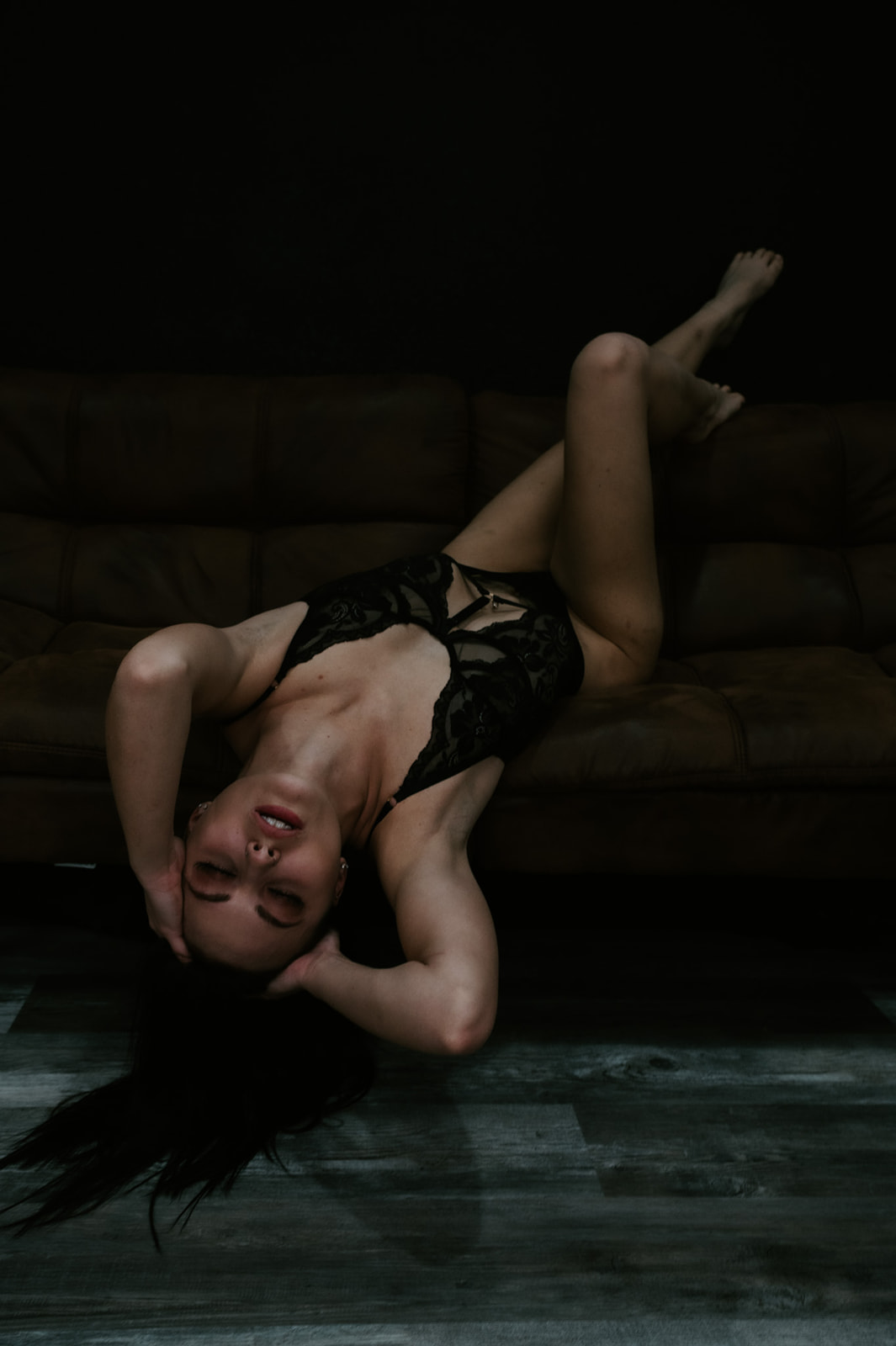 Bride posed upside down on a couch during a boudoir photo shoot, relaxed expression and soft shadows emphasizing comfort