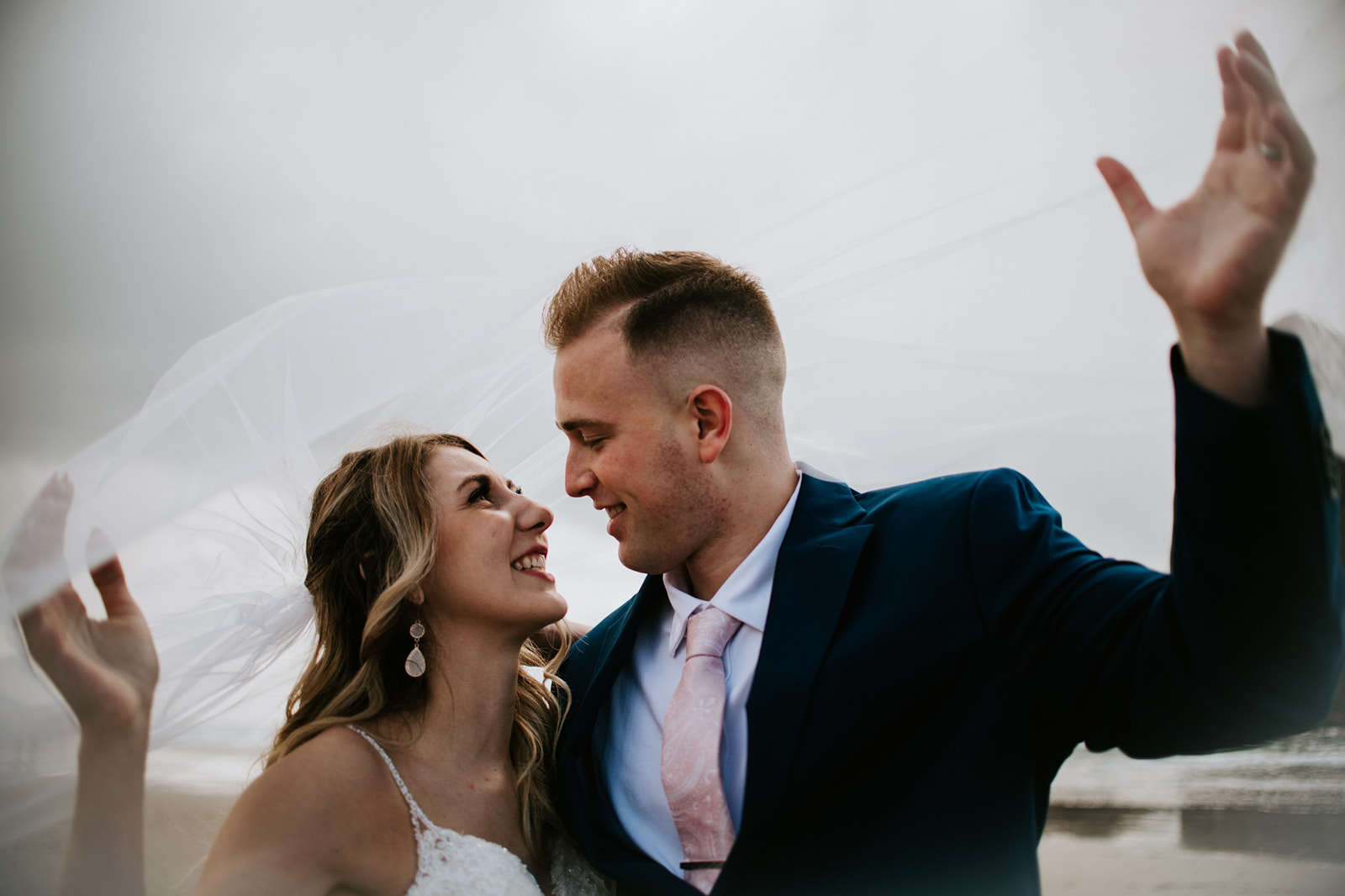 Newly married couple look at one another smiling under bride's veil. 
