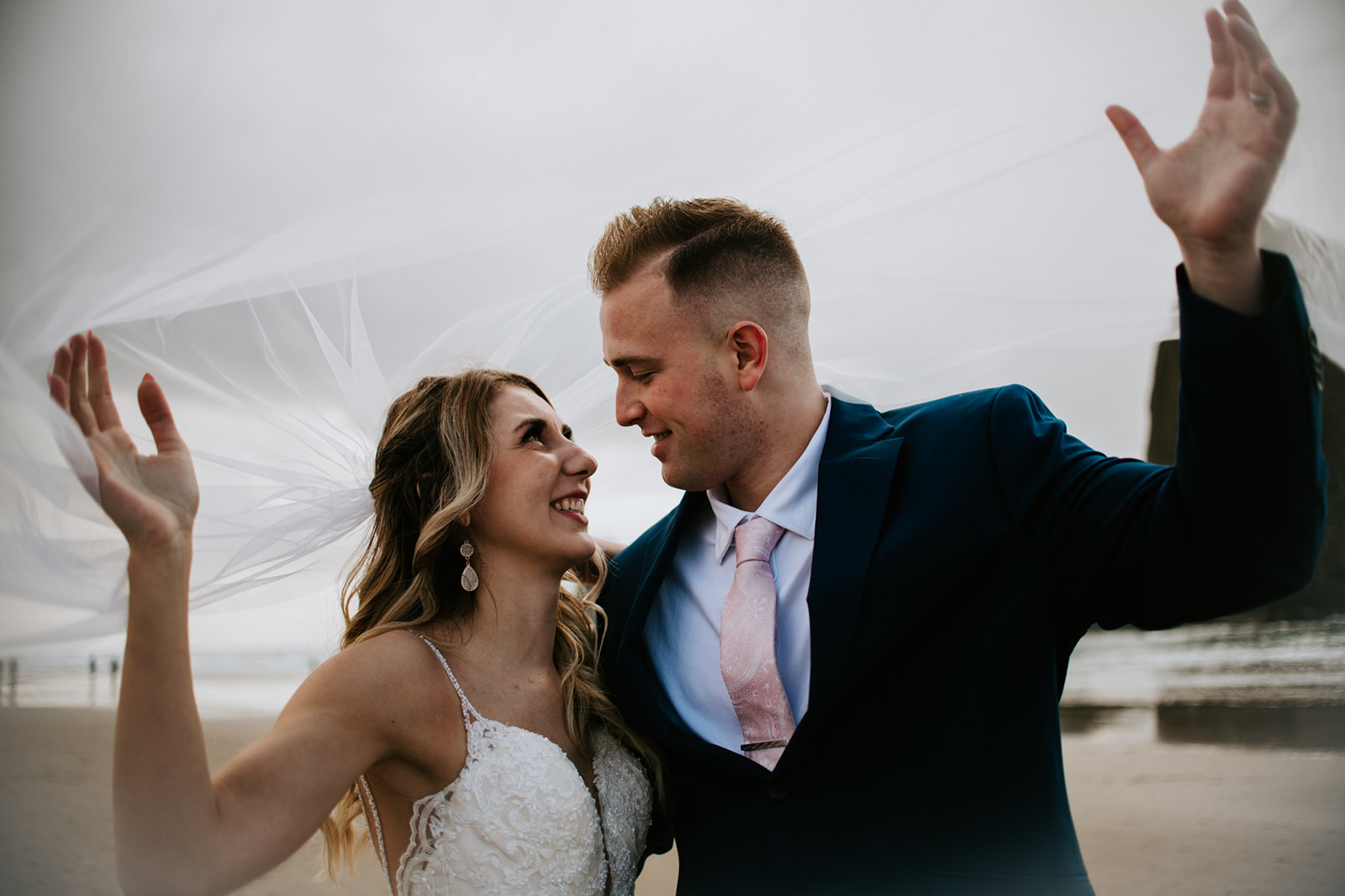 Newly married couple lifting veil and looking at one another after Cannon beach elopement