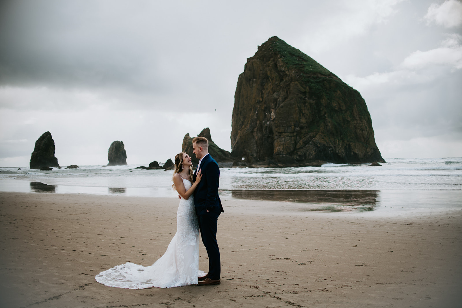 Couple embracing on sandy beach of Cannon Beach with Haystack Rock in the background. 