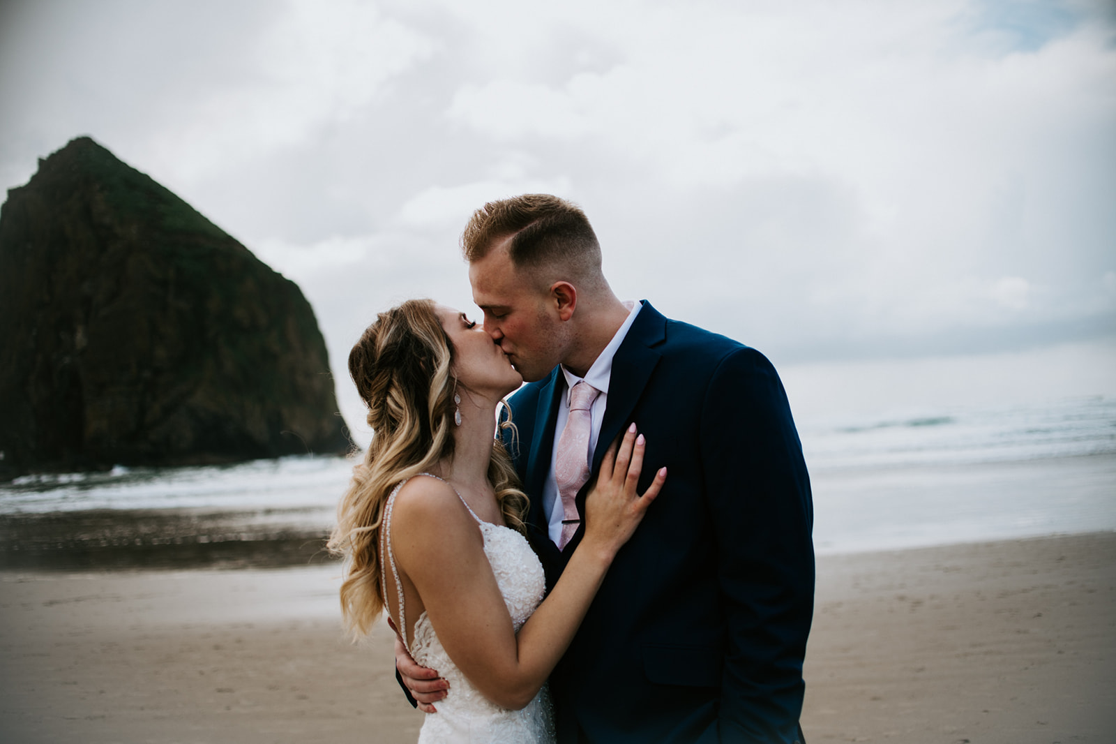 Groom leans down to kiss bride after Oregon elopement on rainy day on Cannon Beach. 