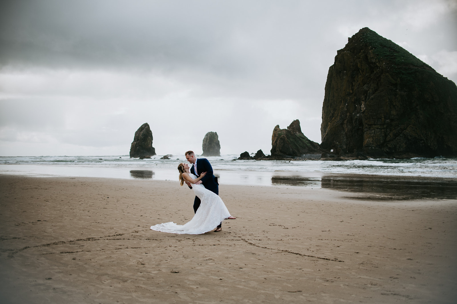 Bride and groom dance on the beaches of Oregon and laugh together celebrating their recent elopement. 