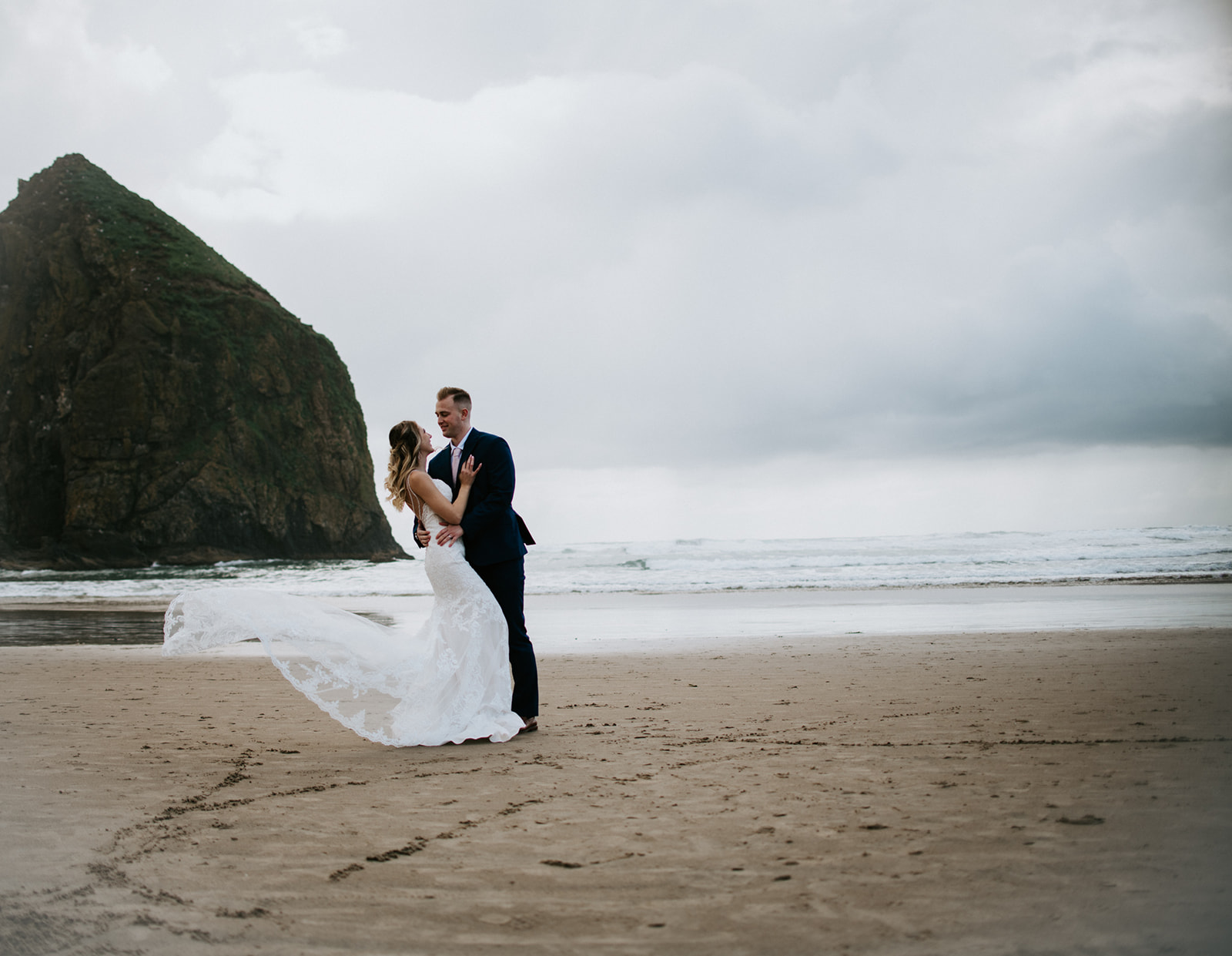 Groom catches bride from falling while dancing together as wind picks up her train. 