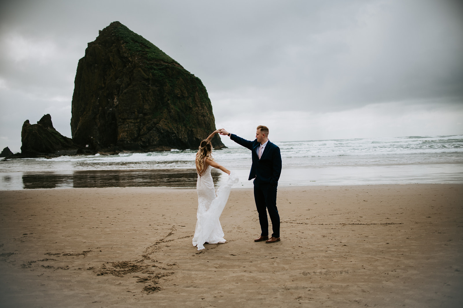 Bride and groom dance together on sandy beach of Oregon coastline. 