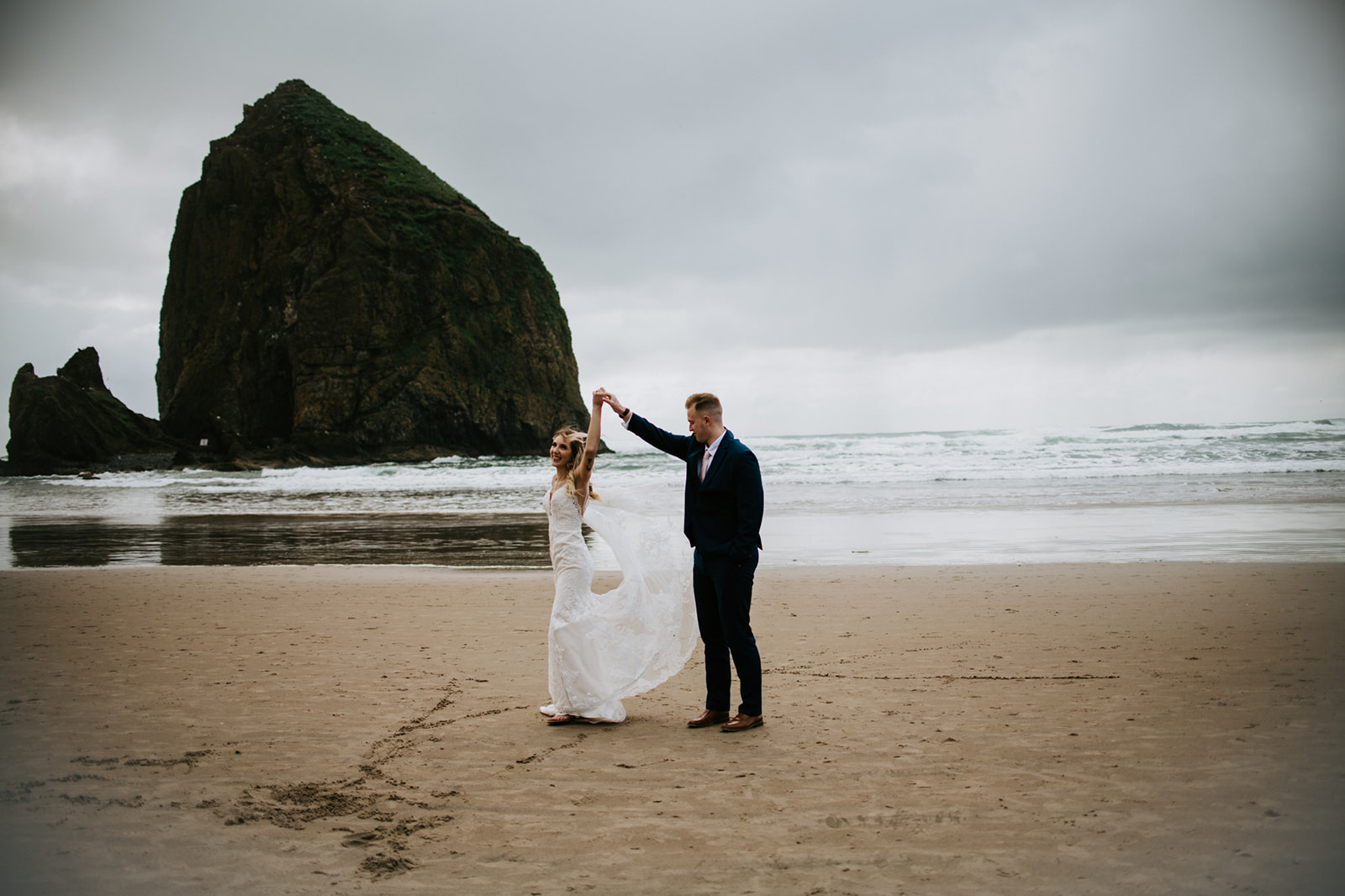 Bride and groom dance in the sand as groom spins bride after Oregon elopement. 