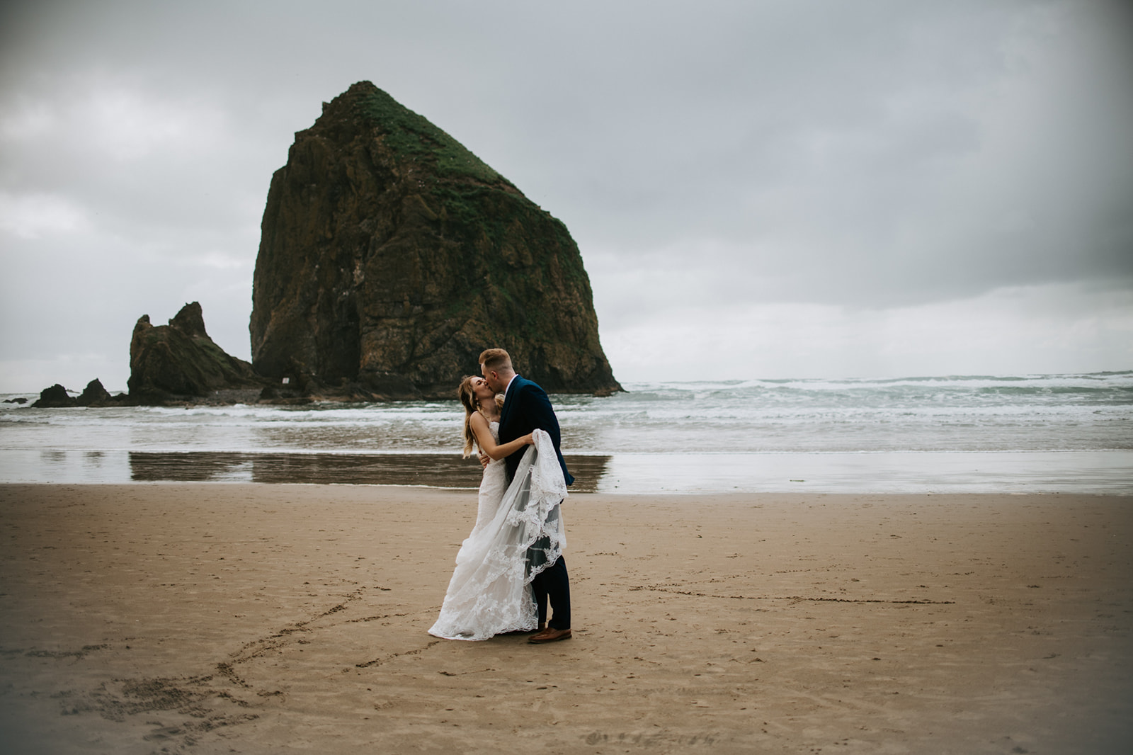 Bride and groom embrace on the sandy beach on Cannon Beach after Oregon Elopement. 