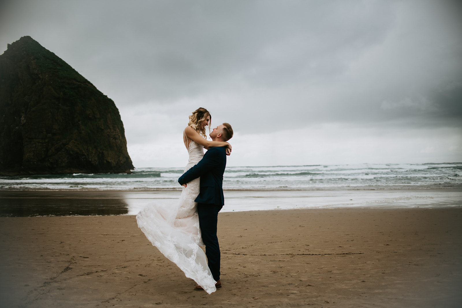 Groom lifts bride in the air to celebrate their recent wedding at Cannon Beach. 
