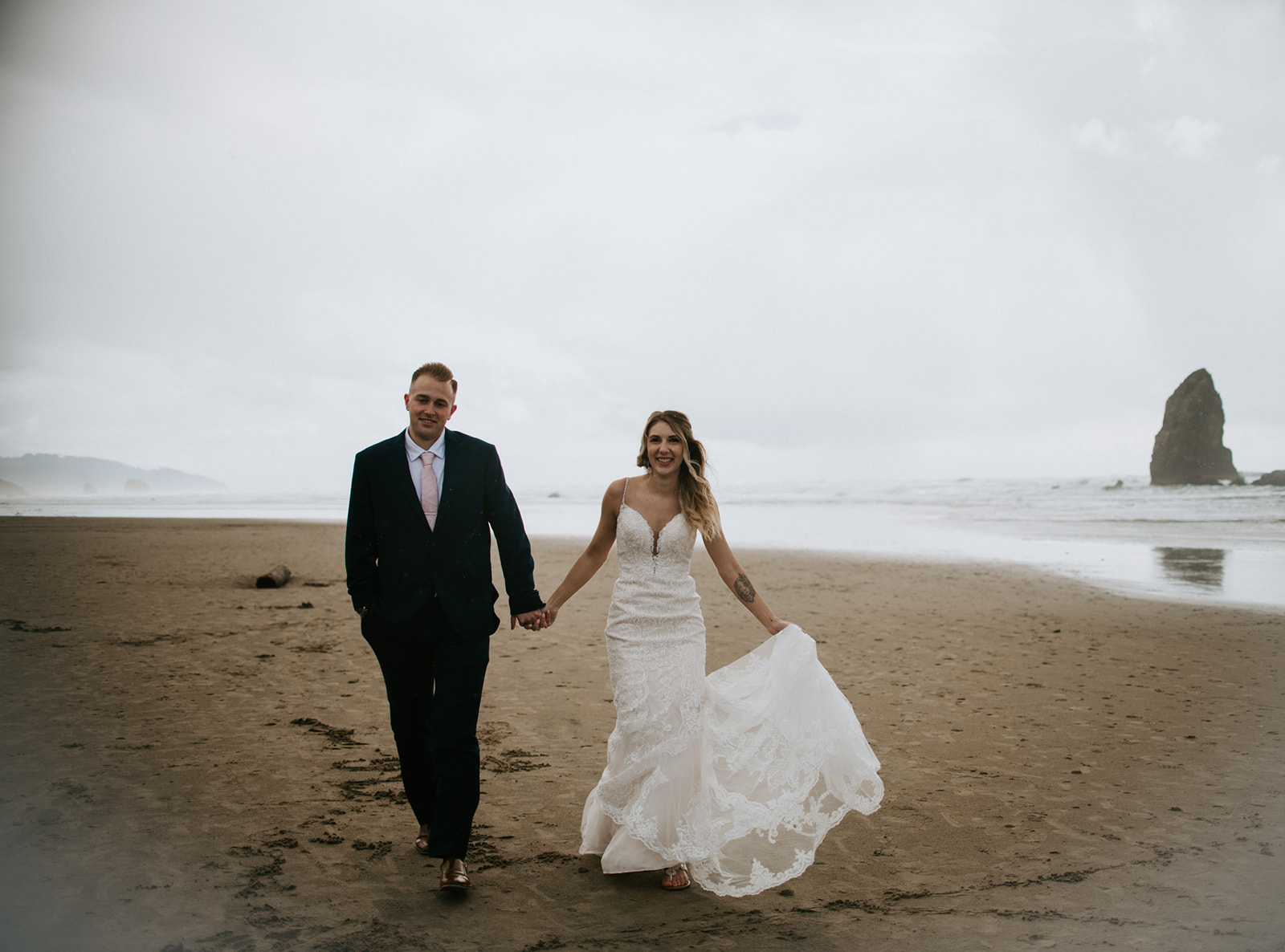 Newly married couple walks hand in hand on the beach together talking and laughing. 
