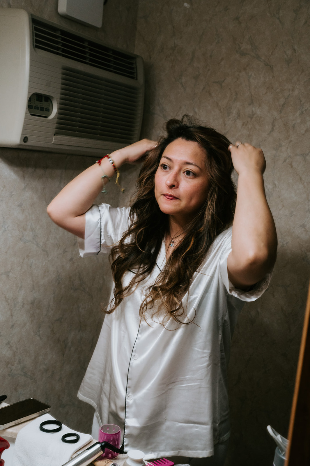 Bride adjusting her hair in the bathroom mirror while getting ready for her winter elopement.